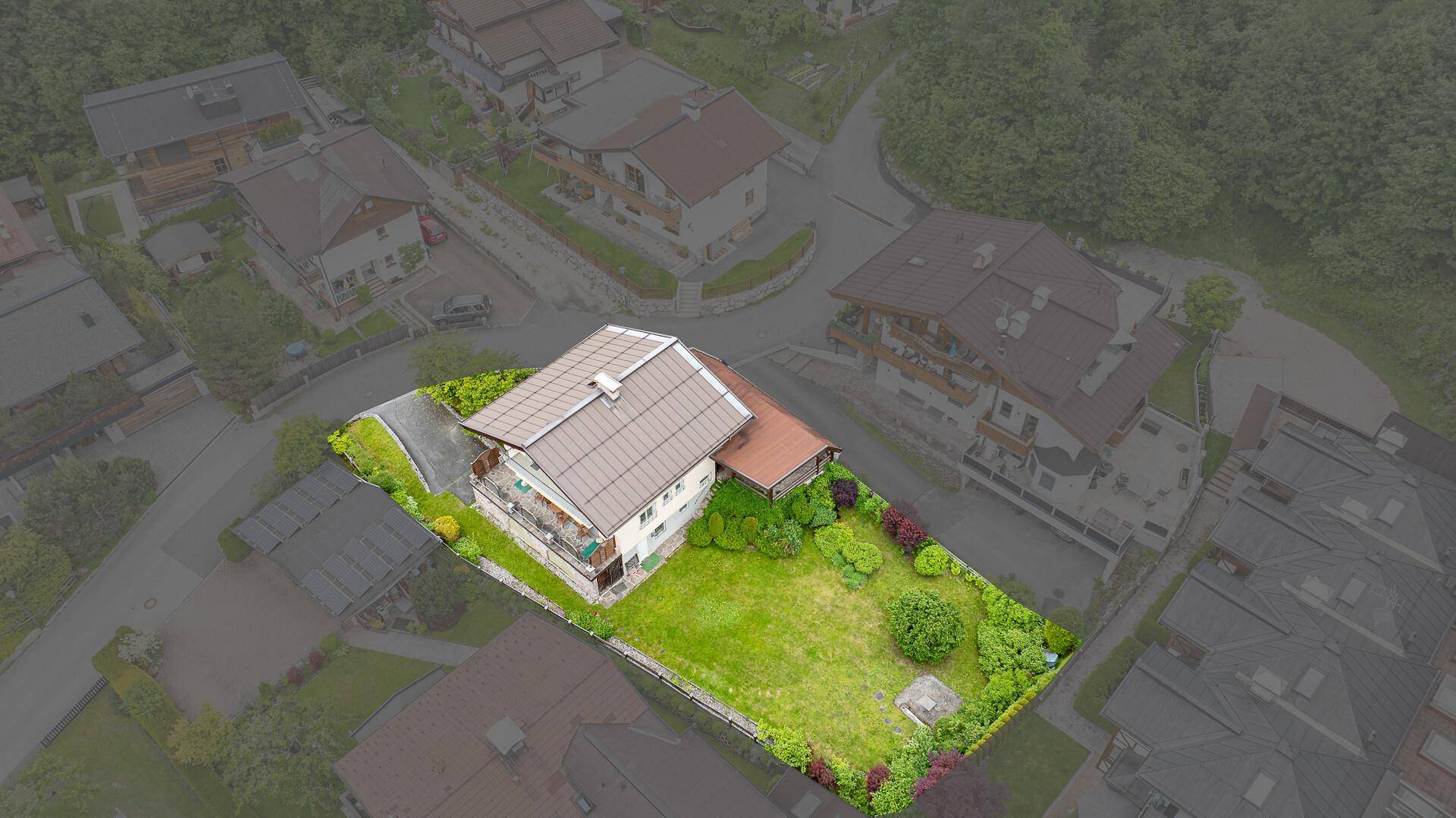 Luftaufnahme eines Grundstücks mit Wohnhaus, großem Garten und Zufahrt, umgeben von weiteren Häusern.