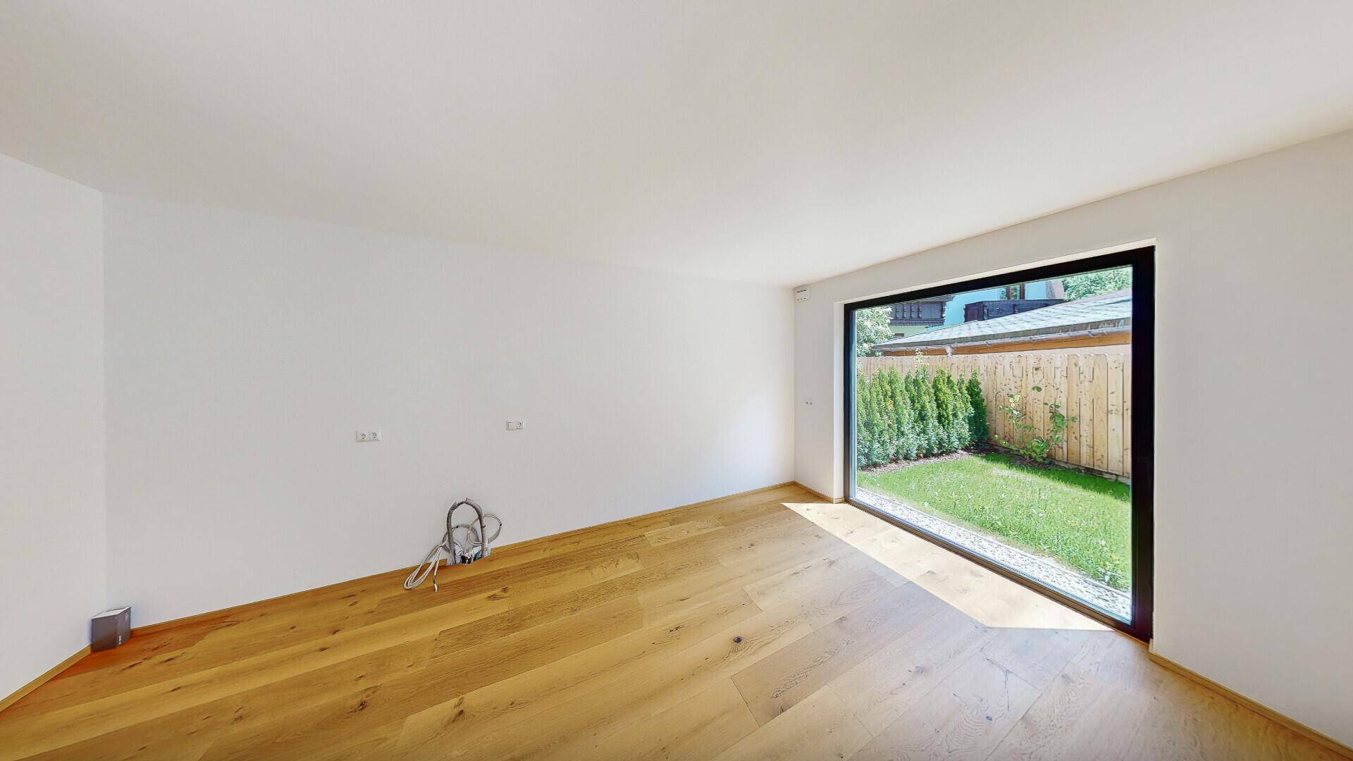 Heller Raum mit Holzboden und einem großen Fenster, das einen schönen Blick auf den Garten bietet.