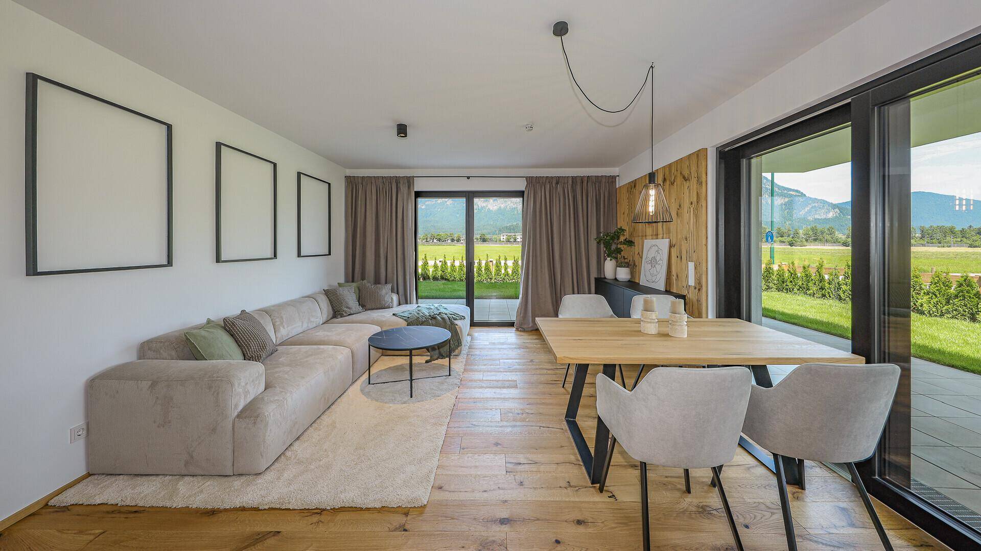 Lichtdurchfluteter Wohn-Essbereich mit gemütlichem Sofa, Holzboden und Blick ins Grüne.