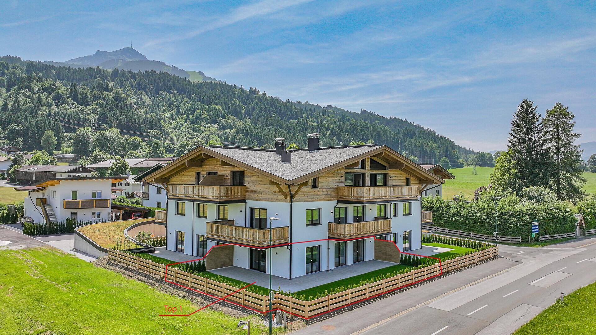 Neubau-Wohnhaus im alpinen Stil mit Balkonen und umzäuntem Gartenbereich in ländlicher Umgebung.