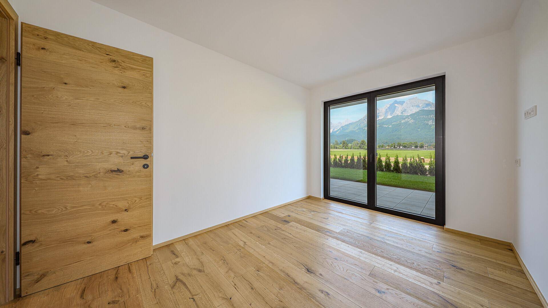 Leeres Schlafzimmer mit Holzboden und großen Fenstern mit Bergblick.