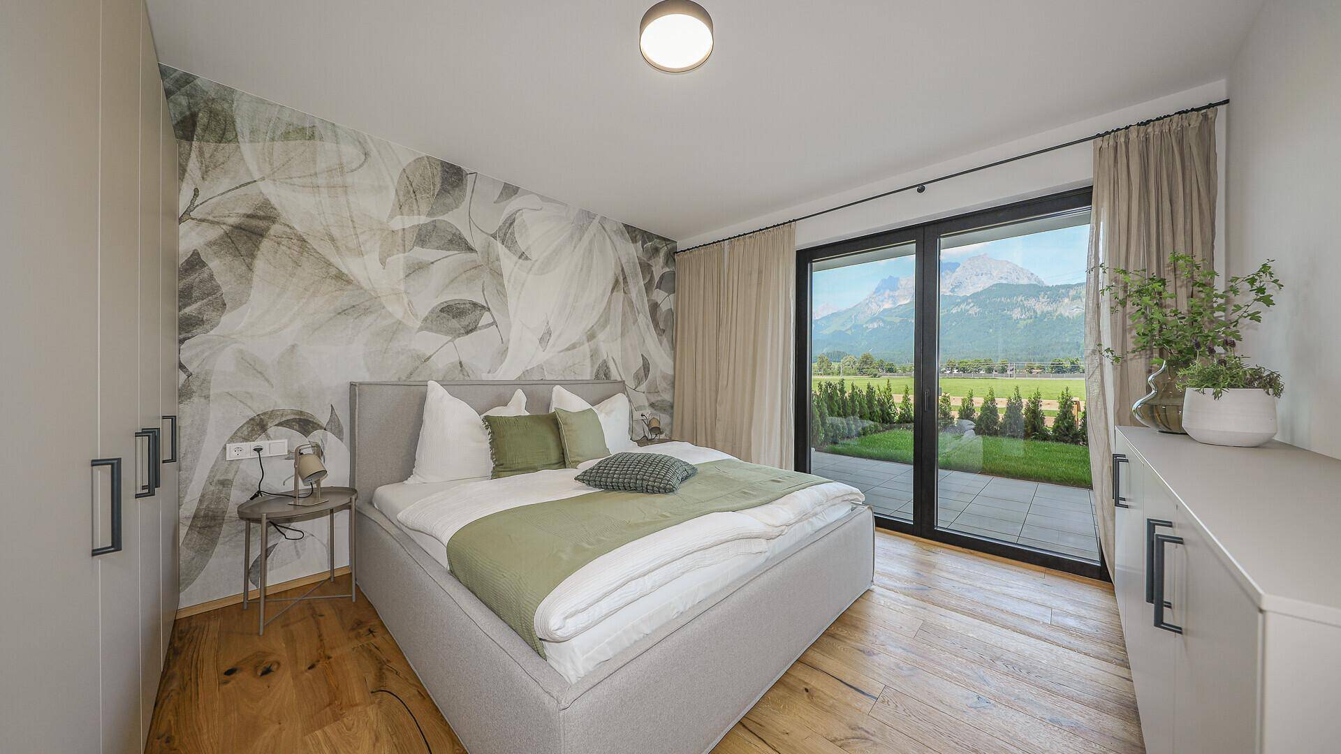 Helles Schlafzimmer mit Doppelbett, Holzboden und Zugang zur Terrasse mit Bergblick.