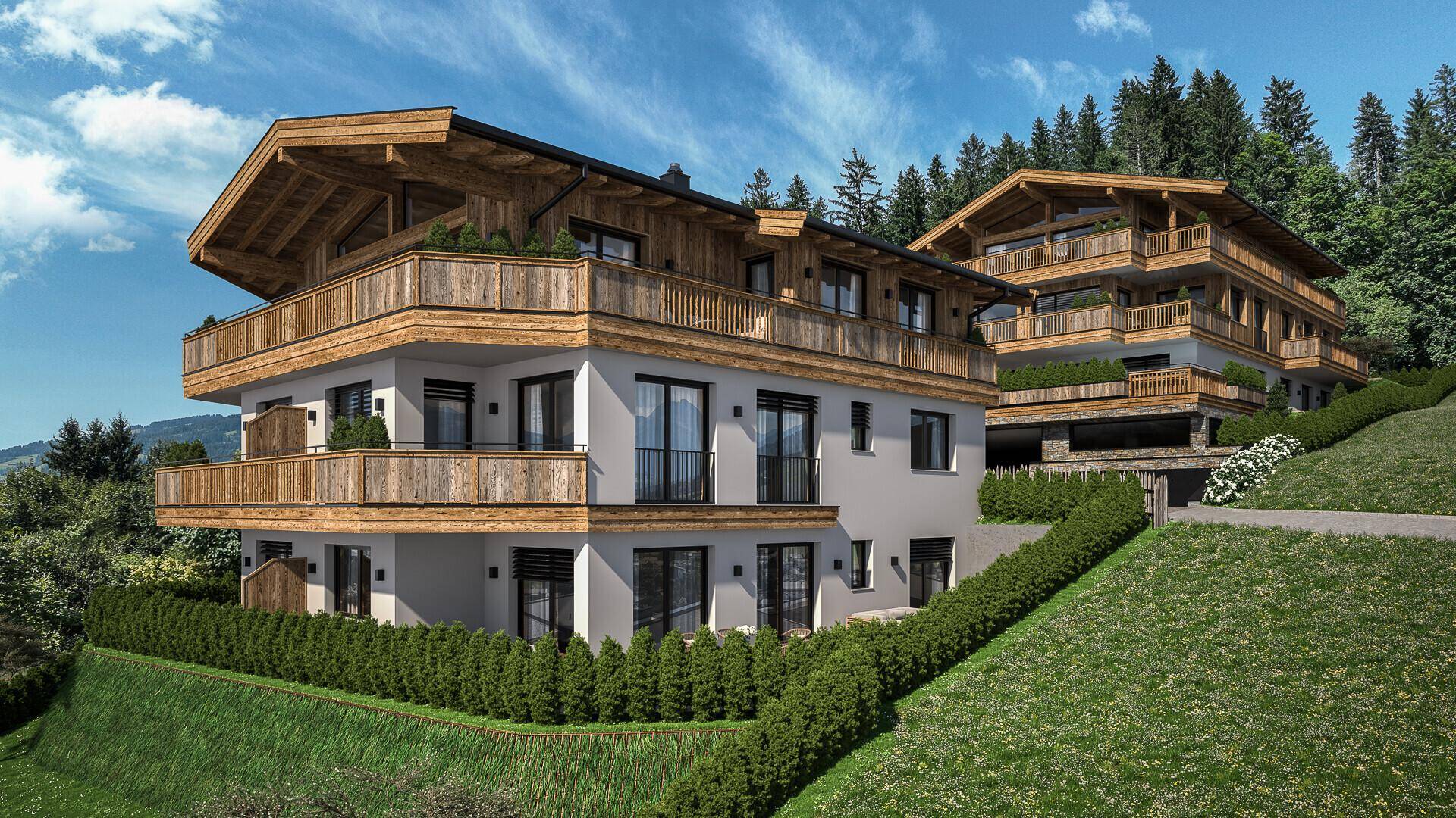 Zwei moderne Chalet-Gebäude mit Holzfassaden und Balkonen, eingebettet in eine grüne Berglandschaft unter blauem Himmel.