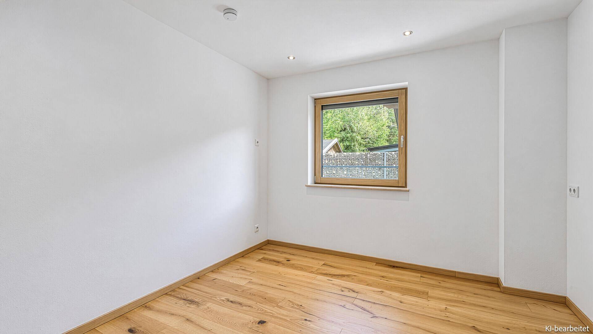 Helles Schlafzimmer mit Holzboden und Fenster mit Blick ins Grüne.