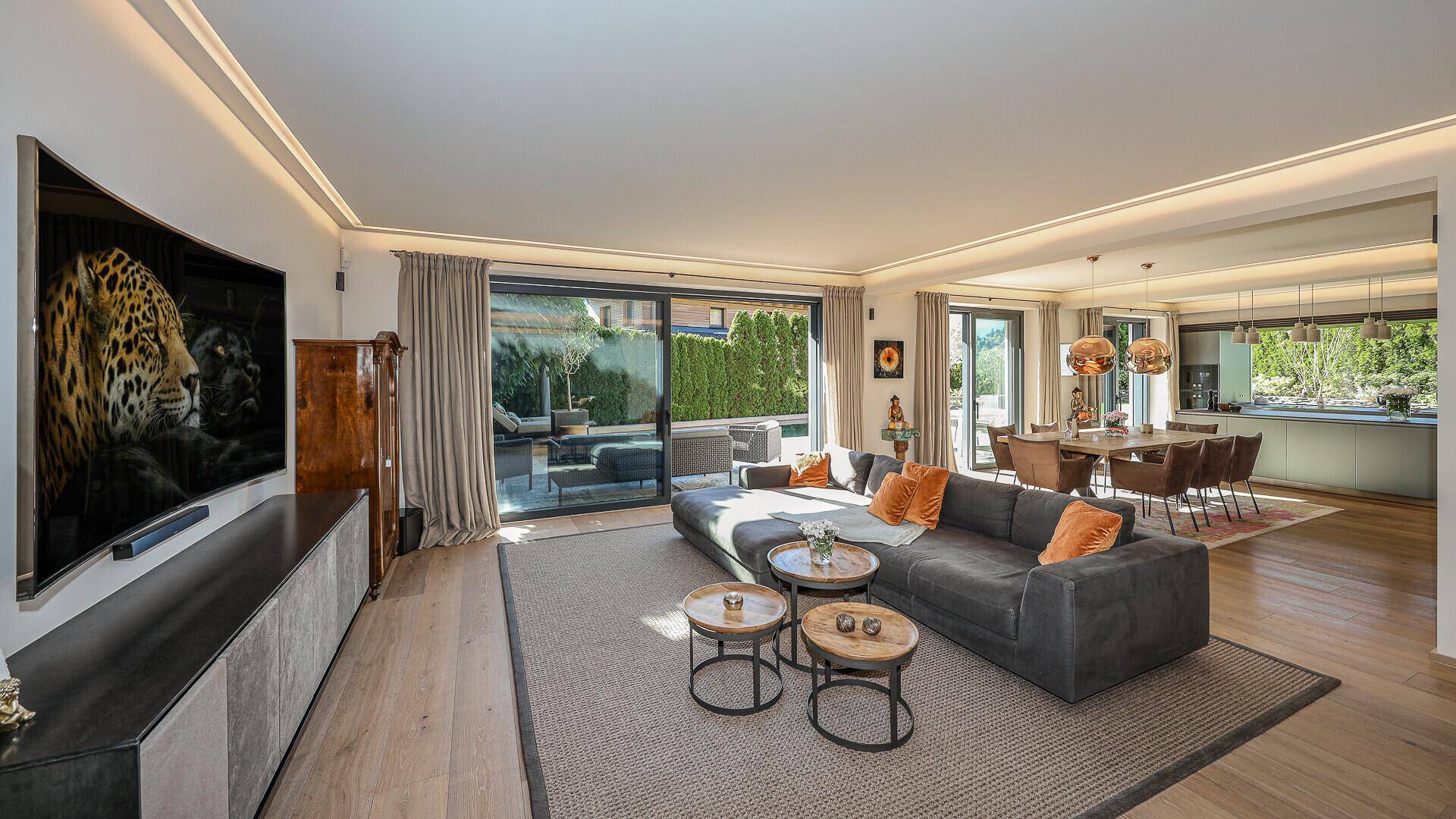 Heller Wohnbereich mit großem Sofa, Fernseher und Zugang zur Terrasse mit Gartenblick.