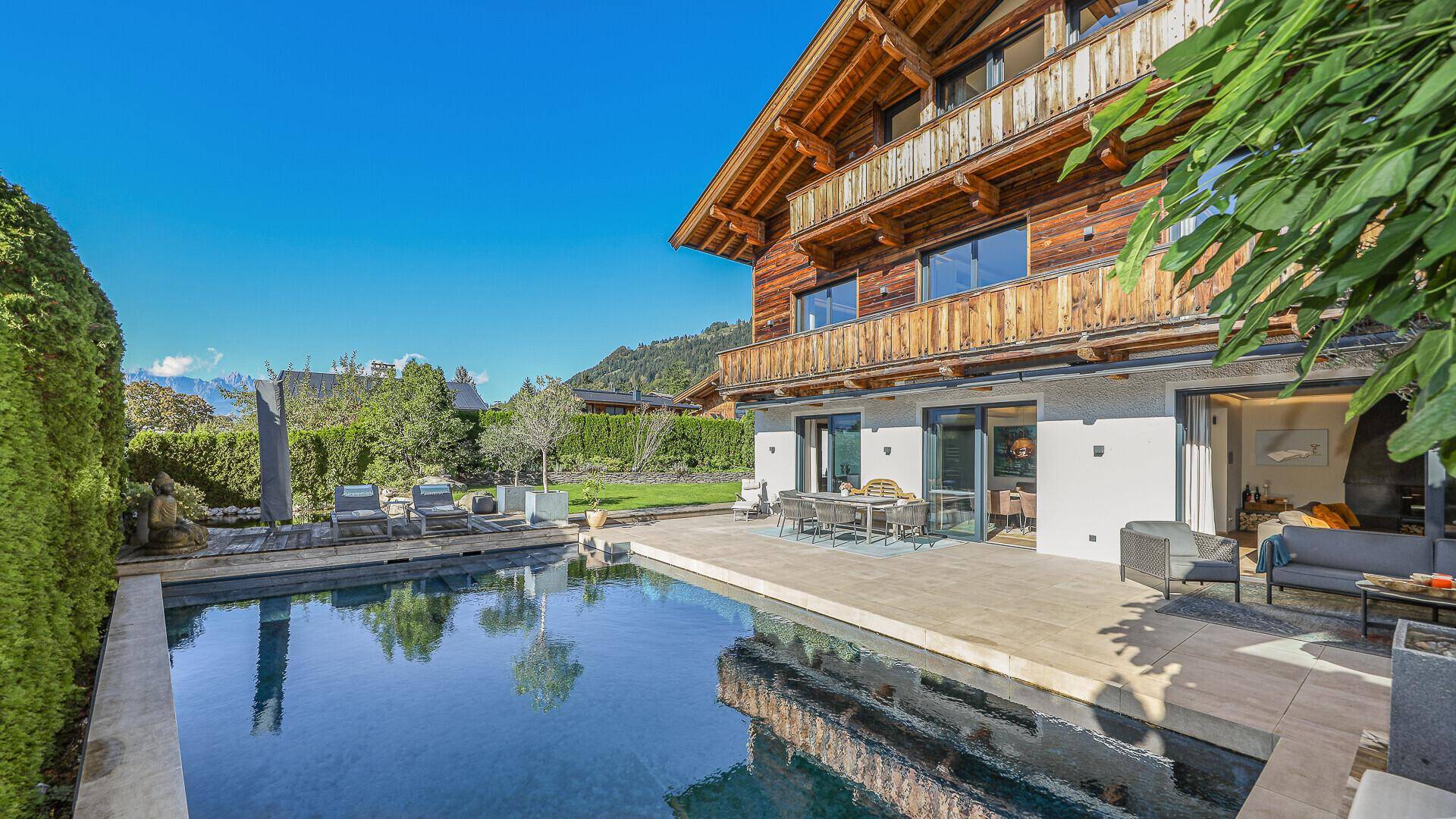 Sonniger Gartenbereich mit großem Pool, Terrasse und Blick auf die umliegende Natur.