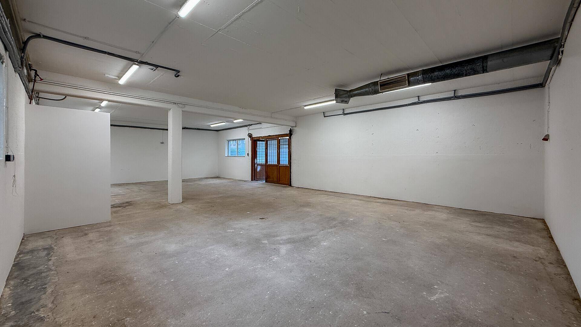 Großer, heller Raum mit Betonboden, weißen Wänden und einer breiten Holztür.