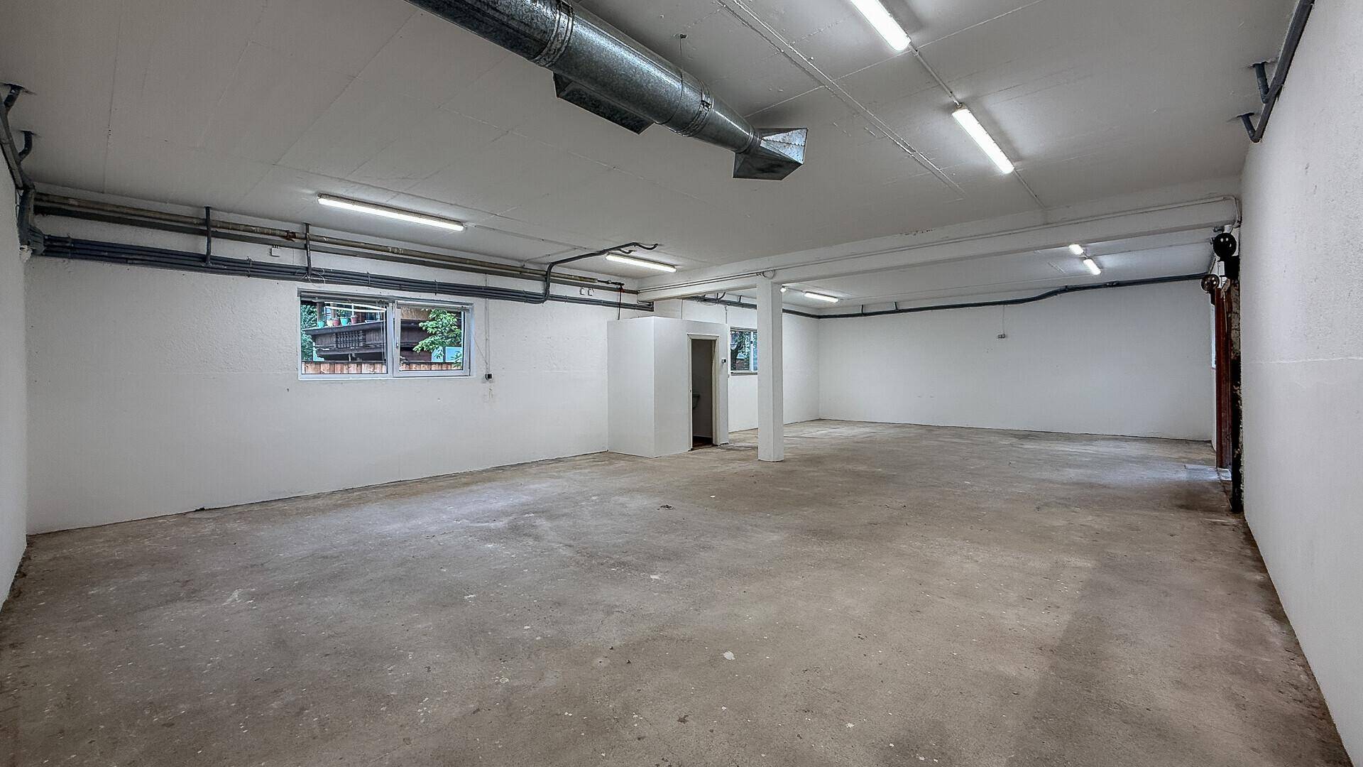 Geräumiger Innenraum mit sichtbaren Lüftungsrohren an der Decke und Betonboden.