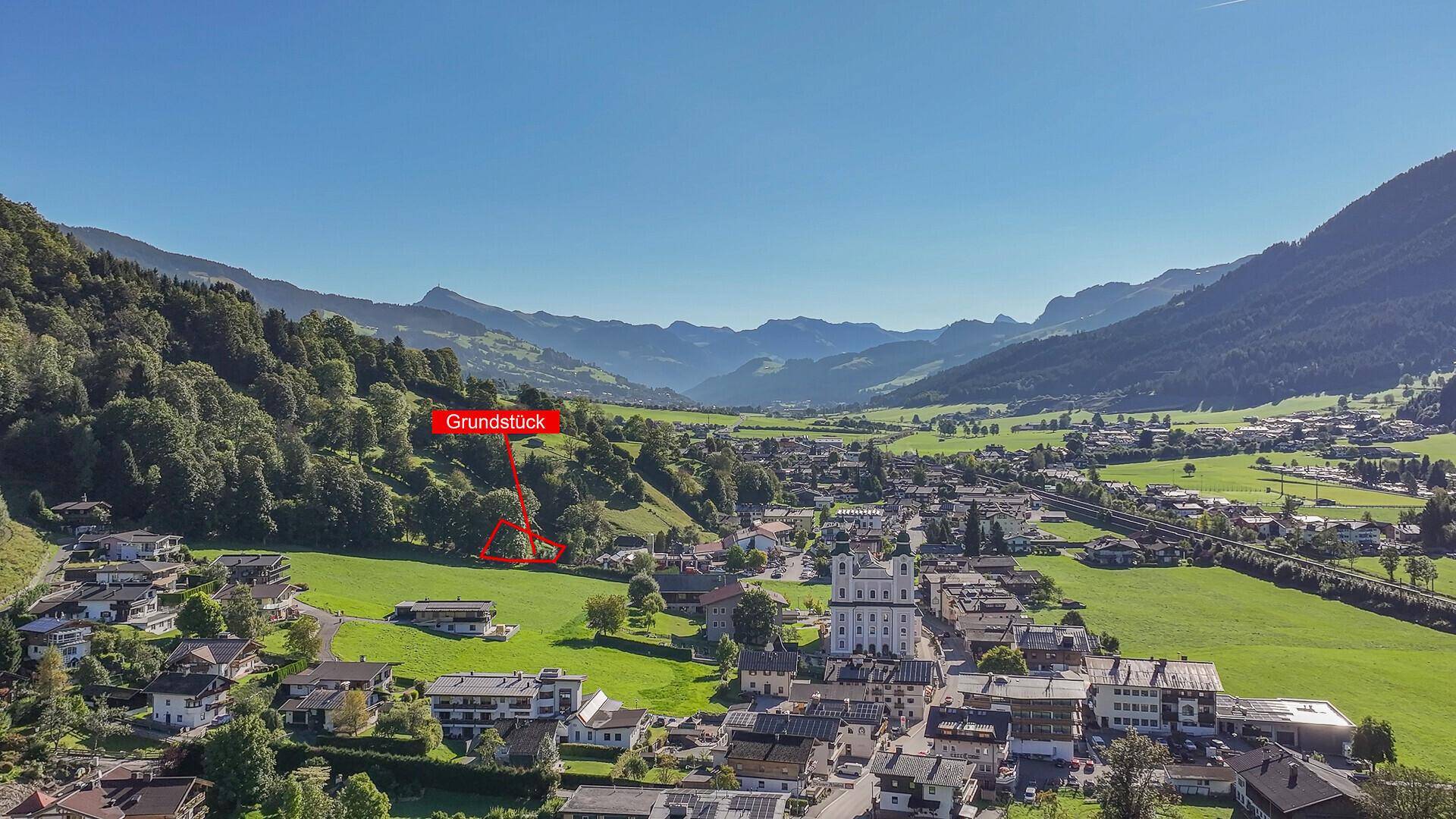 Weitläufige Luftaufnahme eines Grundstücks in einer idyllischen Berglandschaft mit Dorfansicht.