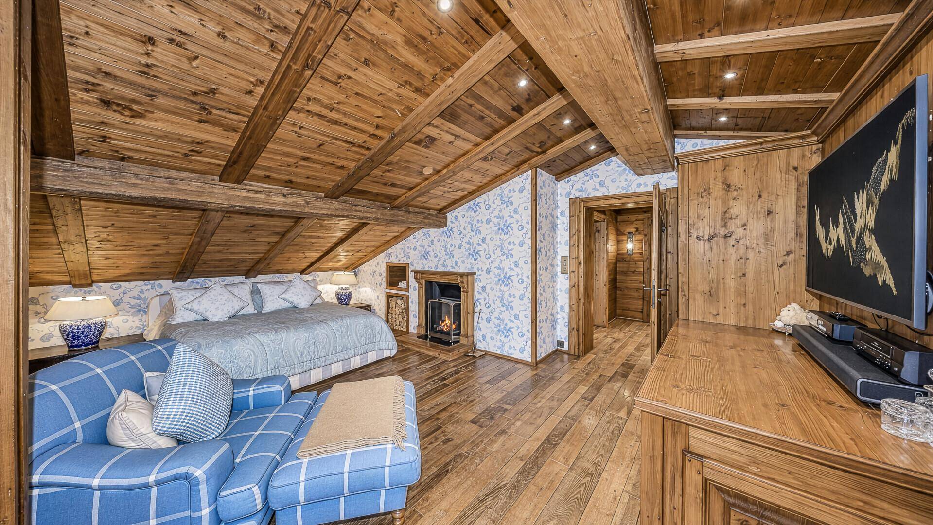 Gemütliches Schlafzimmer im Dachgeschoss mit Holzbalkendecke, Kamin und floraler Tapete.