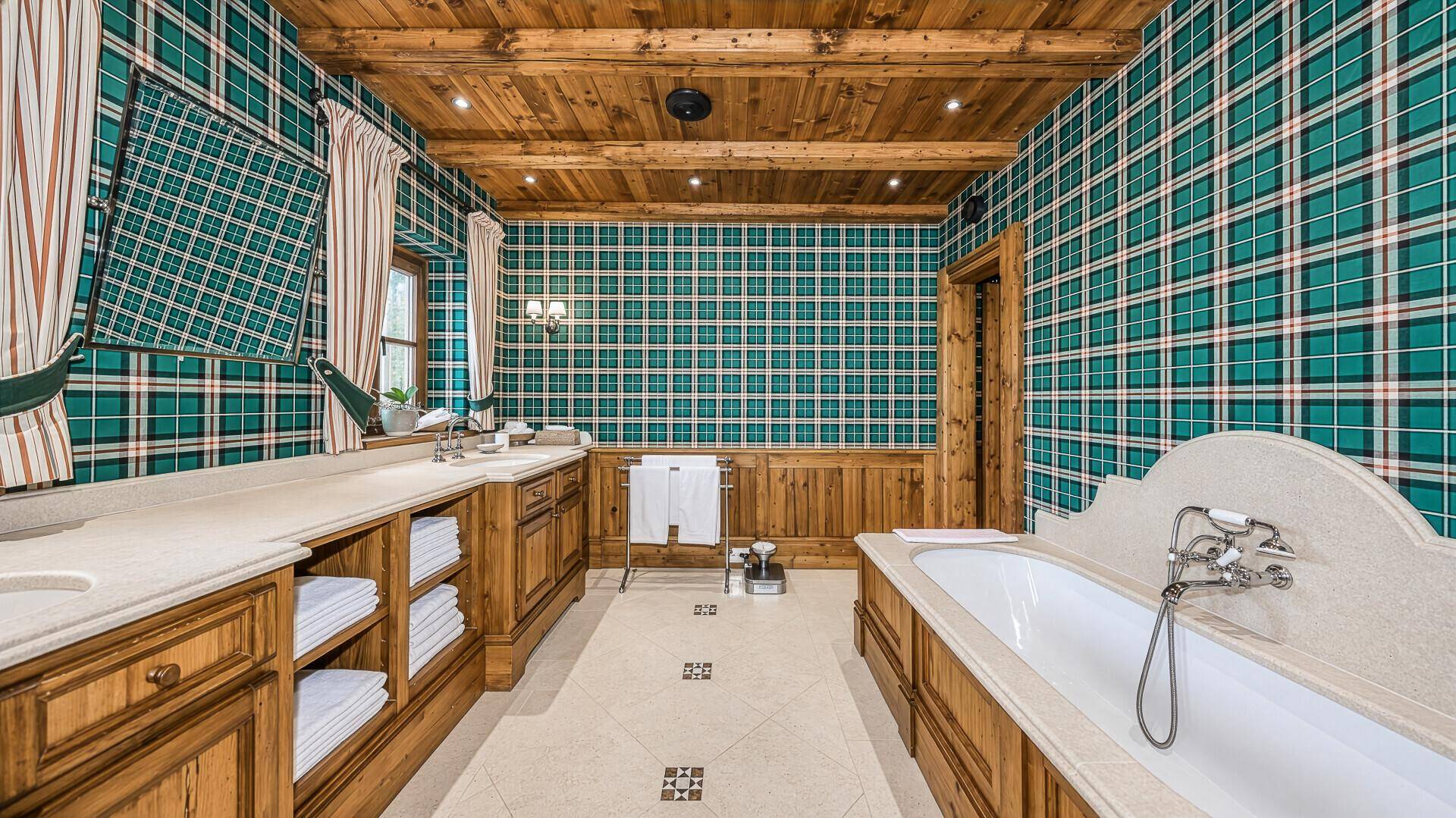 Geräumiges Badezimmer mit Holzbalkendecke, karierter Tapete und Doppelwaschtisch.