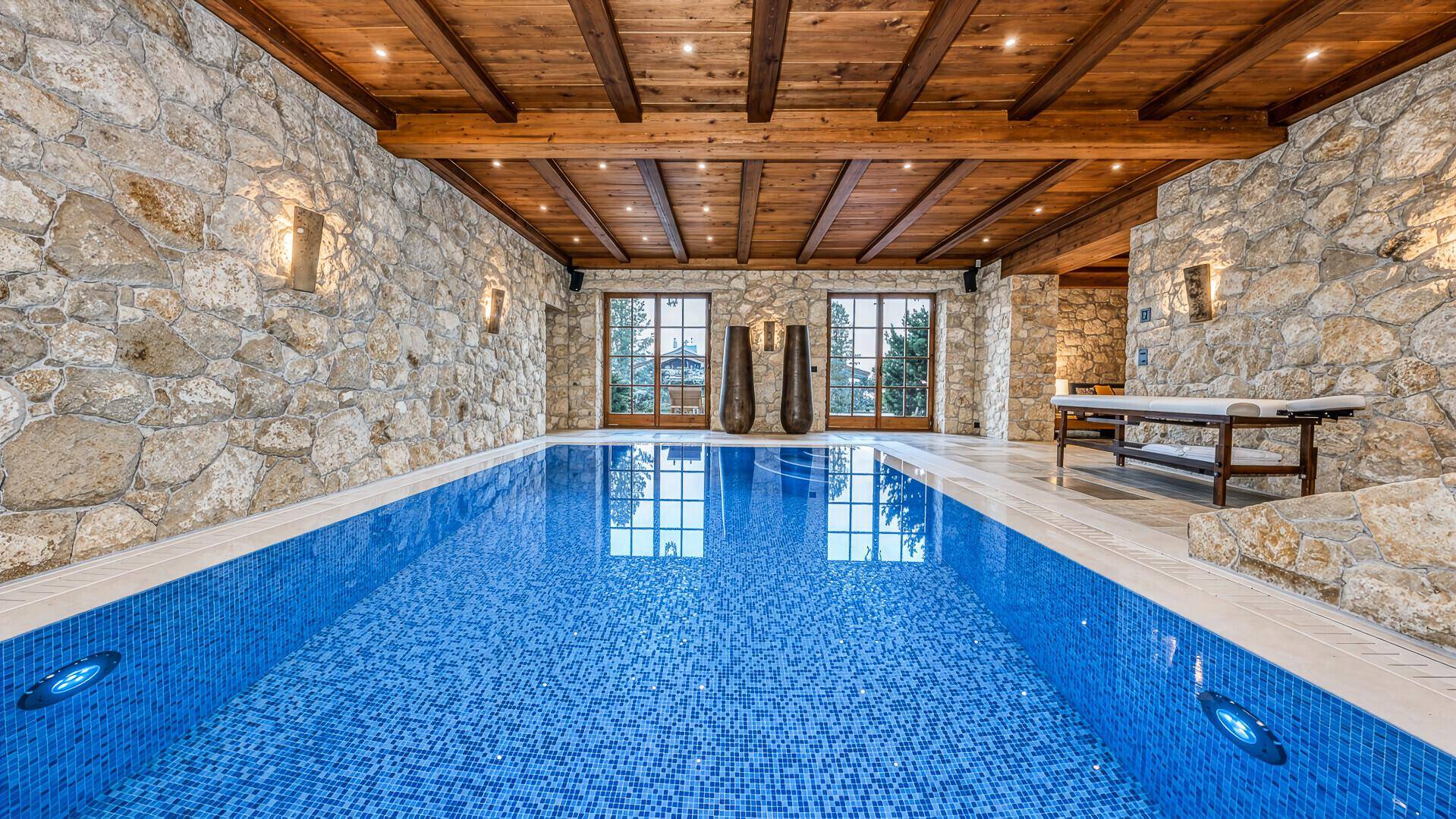 Heller Innenpool mit blauen Mosaikfliesen, Steinwänden und Blick nach draußen.