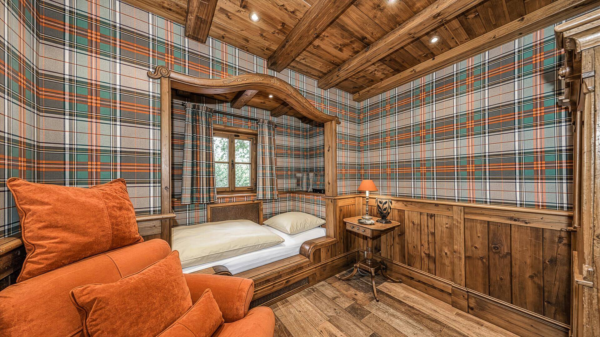 Gemütliches Schlafzimmer im alpinen Stil mit Holzbett, karierter Tapete und sichtbaren Holzbalken.