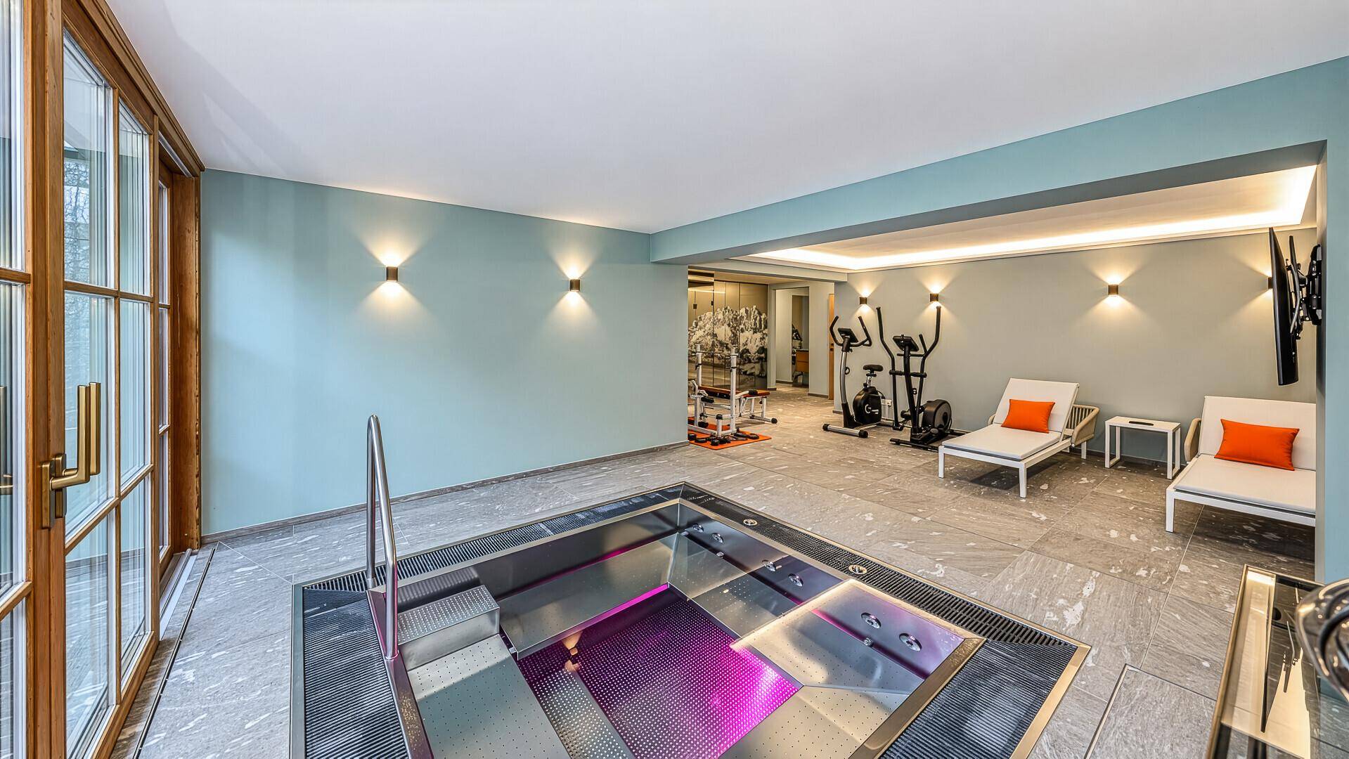 Geräumiger Wellnessbereich mit Innenpool, Fitnessgeräten und großen Fenstern.
