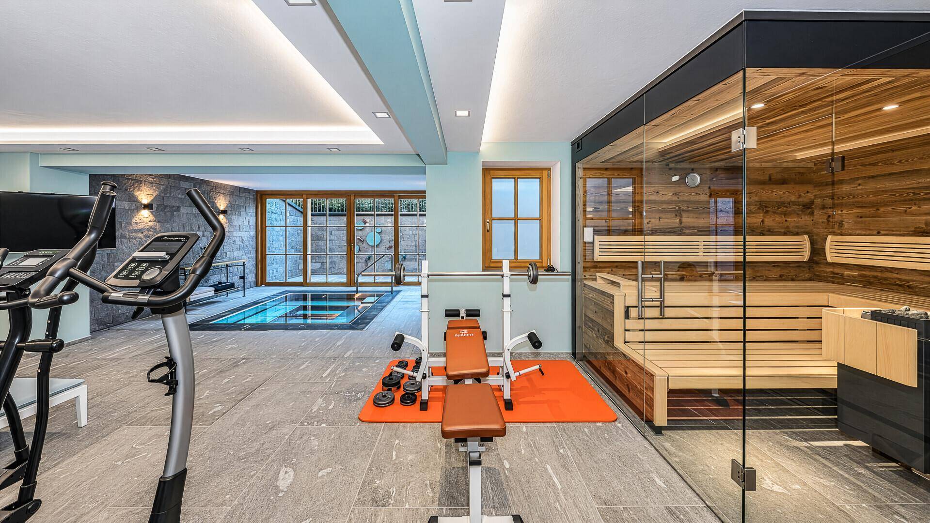 Luxuriöser Wellnessbereich mit Sauna, Fitnessgeräten und Blick auf den Pool.