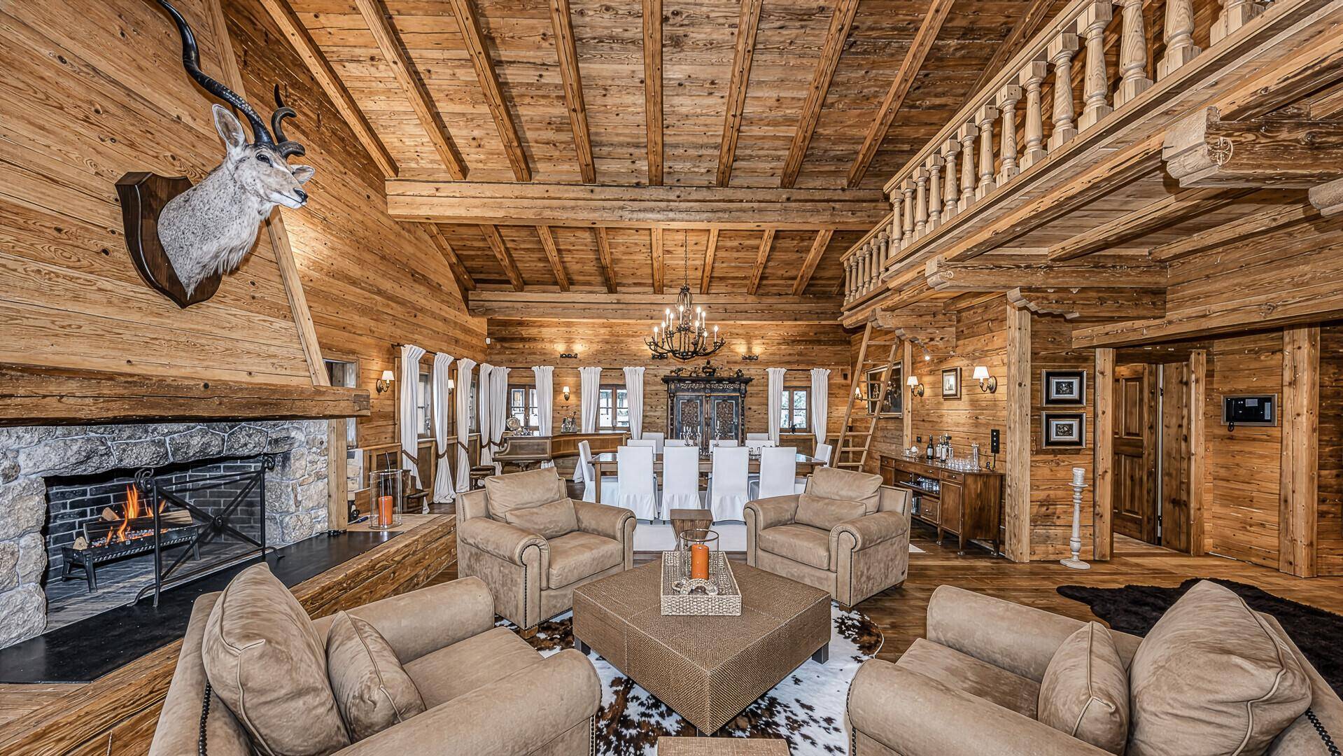 Gemütlicher Wohnbereich im Chalet-Stil mit Steinkamin, Holzwänden und rustikalen Möbeln.