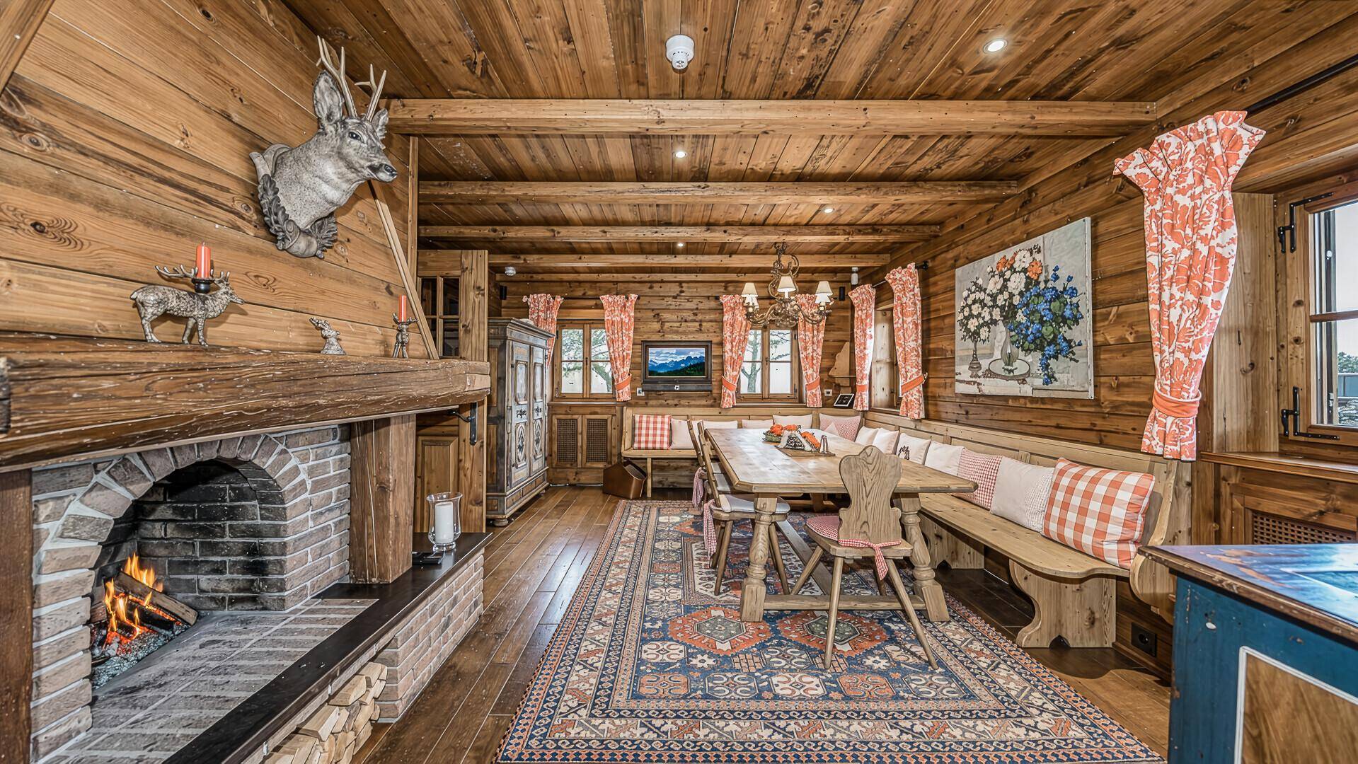 Rustikaler Essbereich mit Kamin, Holzbänken und traditionellen Textilien in warmen Farben.