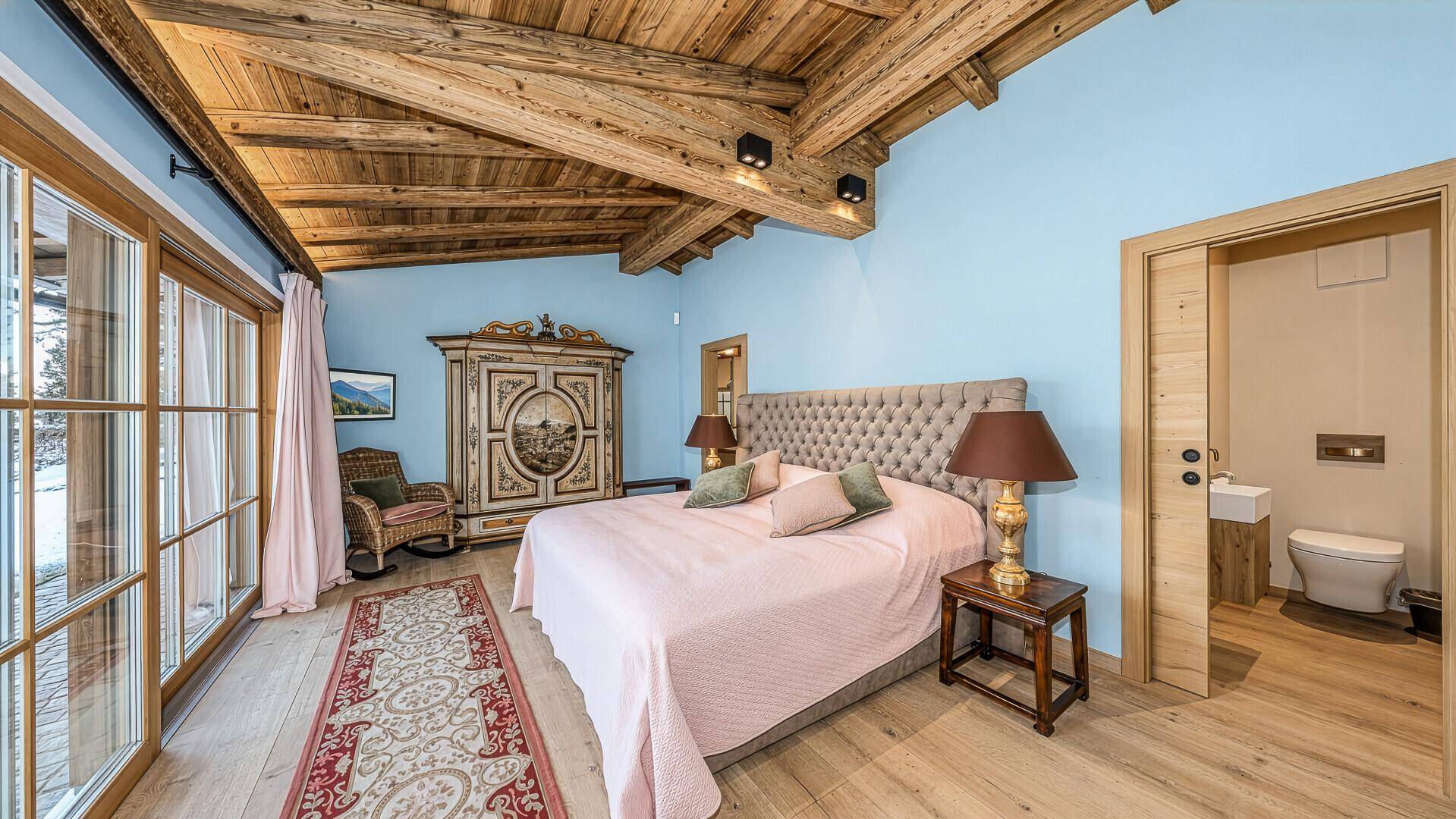 Helles Schlafzimmer mit Holzbalkendecke, Balkonzugang und integriertem WC-Bereich.
