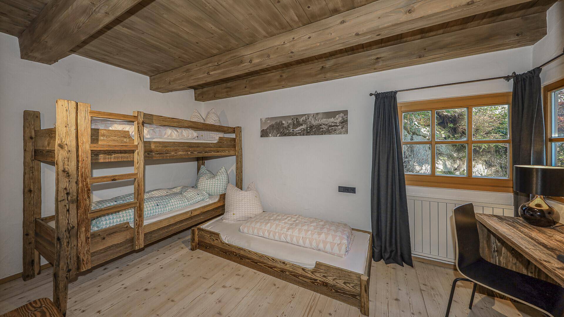 Kinderzimmer mit Etagenbett, Einzelbett und Schreibtisch in rustikalem Holzstil.