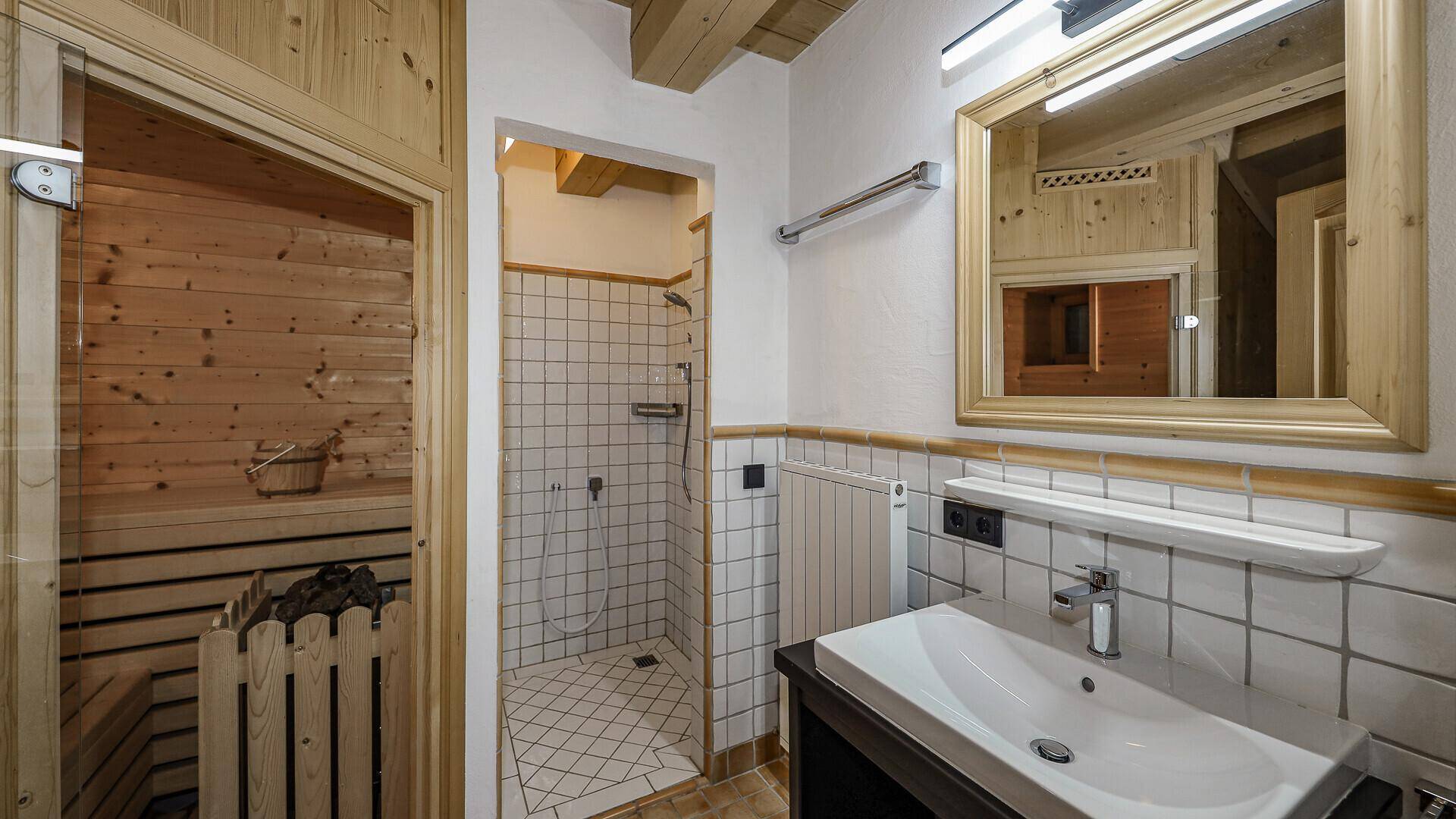 Badezimmer mit Dusche, Waschbecken und direktem Zugang zur Sauna.