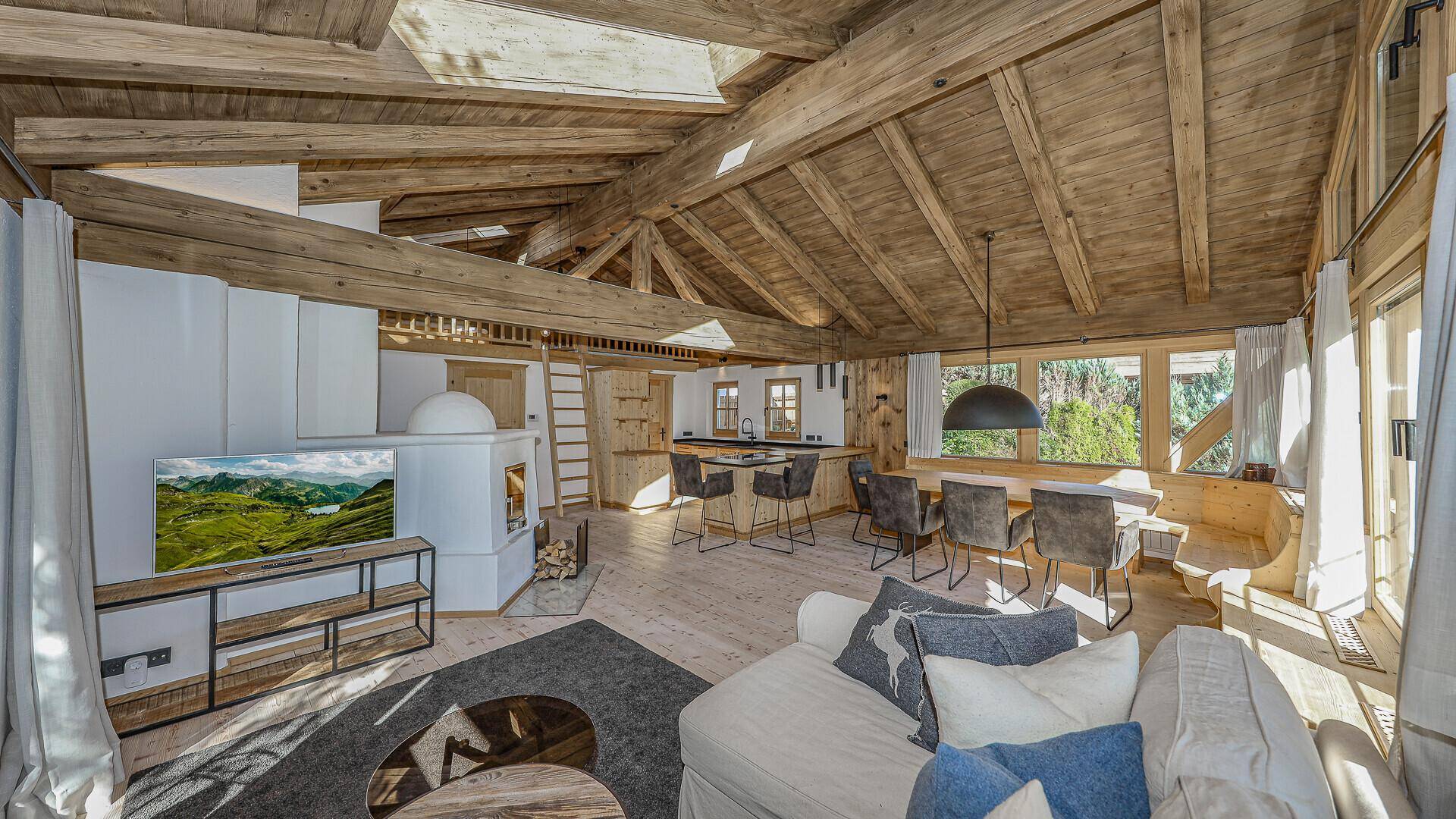 Großzügiger offener Wohnbereich mit Holzbalkendecke, Kamin und integrierter Küche.