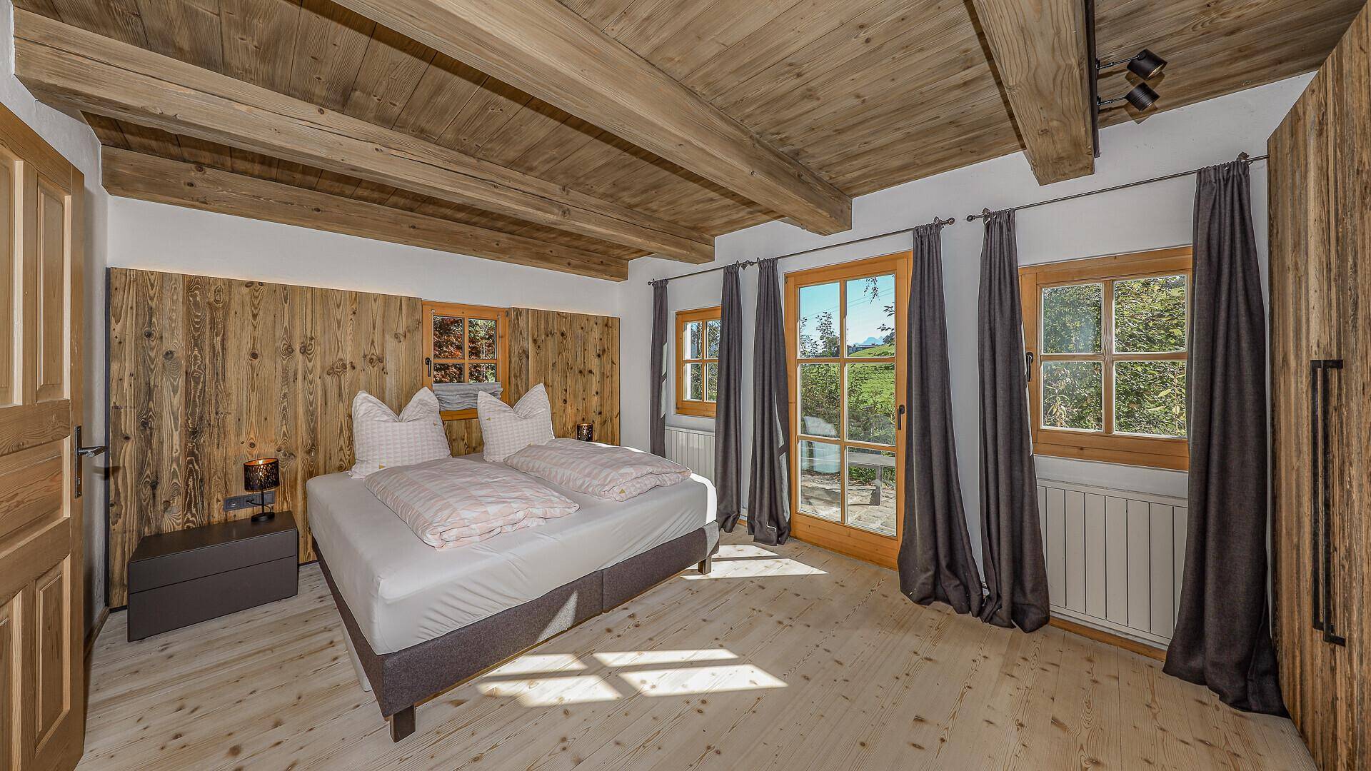 Gemütliches Schlafzimmer mit Holzbalkendecke, Doppelbett und Zugang zum Balkon.