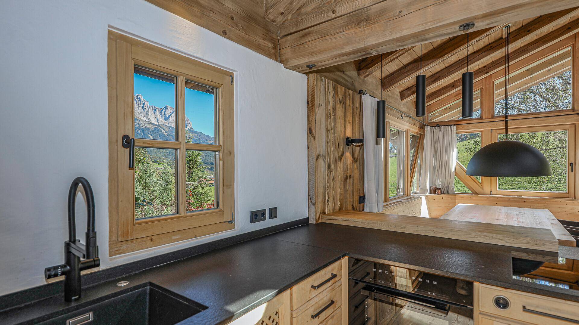 Helle Küche mit Holzfenster, dunkler Arbeitsplatte und Bergblick.