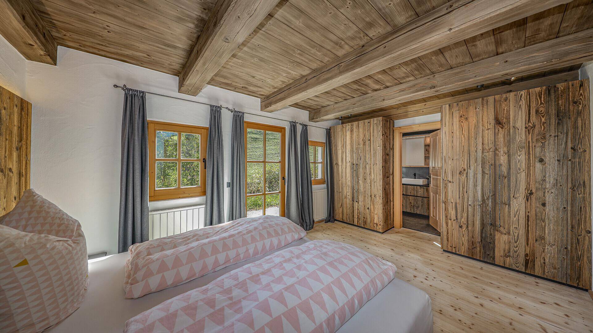Helles Schlafzimmer mit Holzbalkendecke, Einbauschränken und Blick ins Grüne.