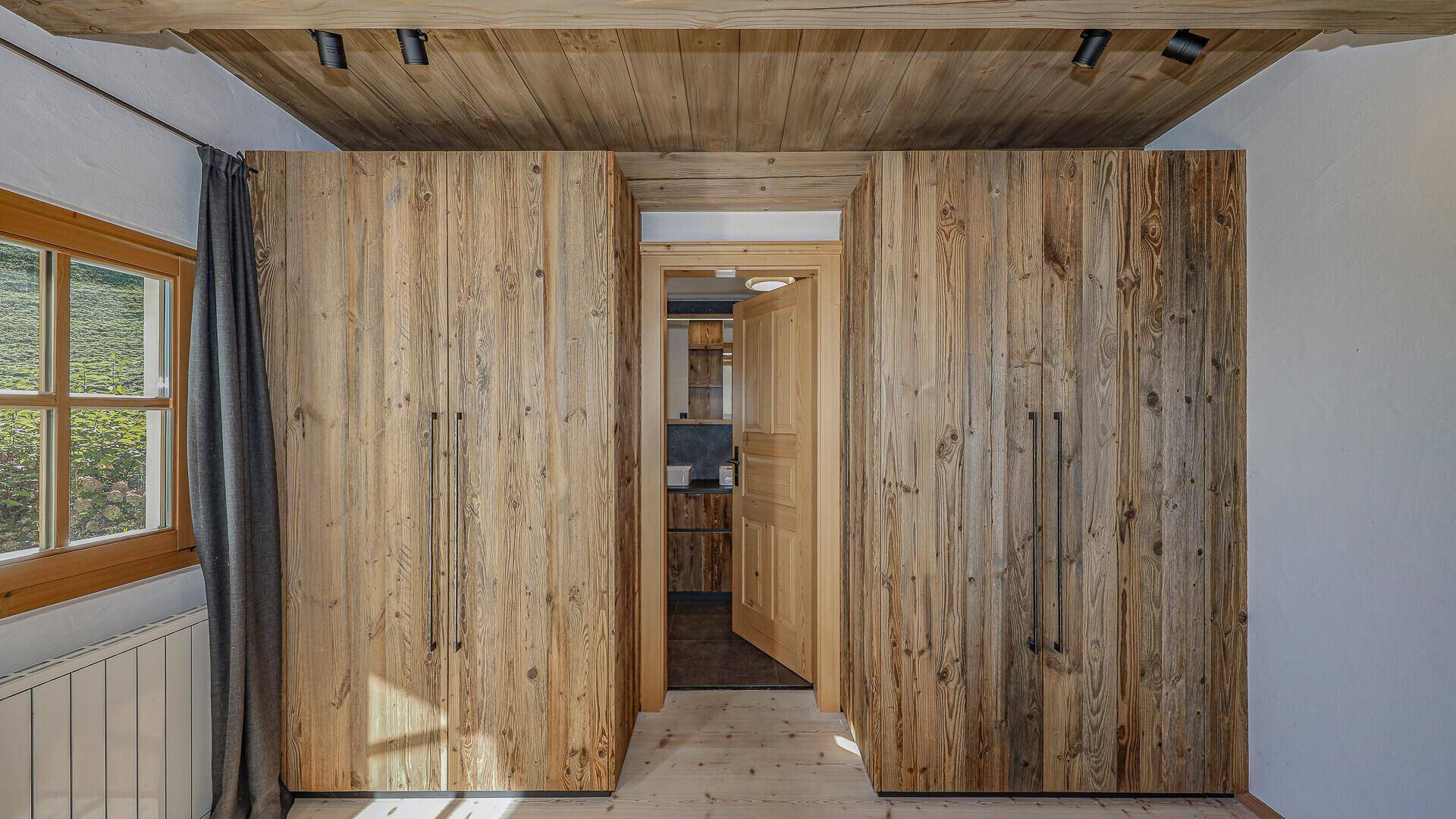 Schlafzimmer mit maßgefertigten Holzschränken und Zugang zu einem weiteren Raum.