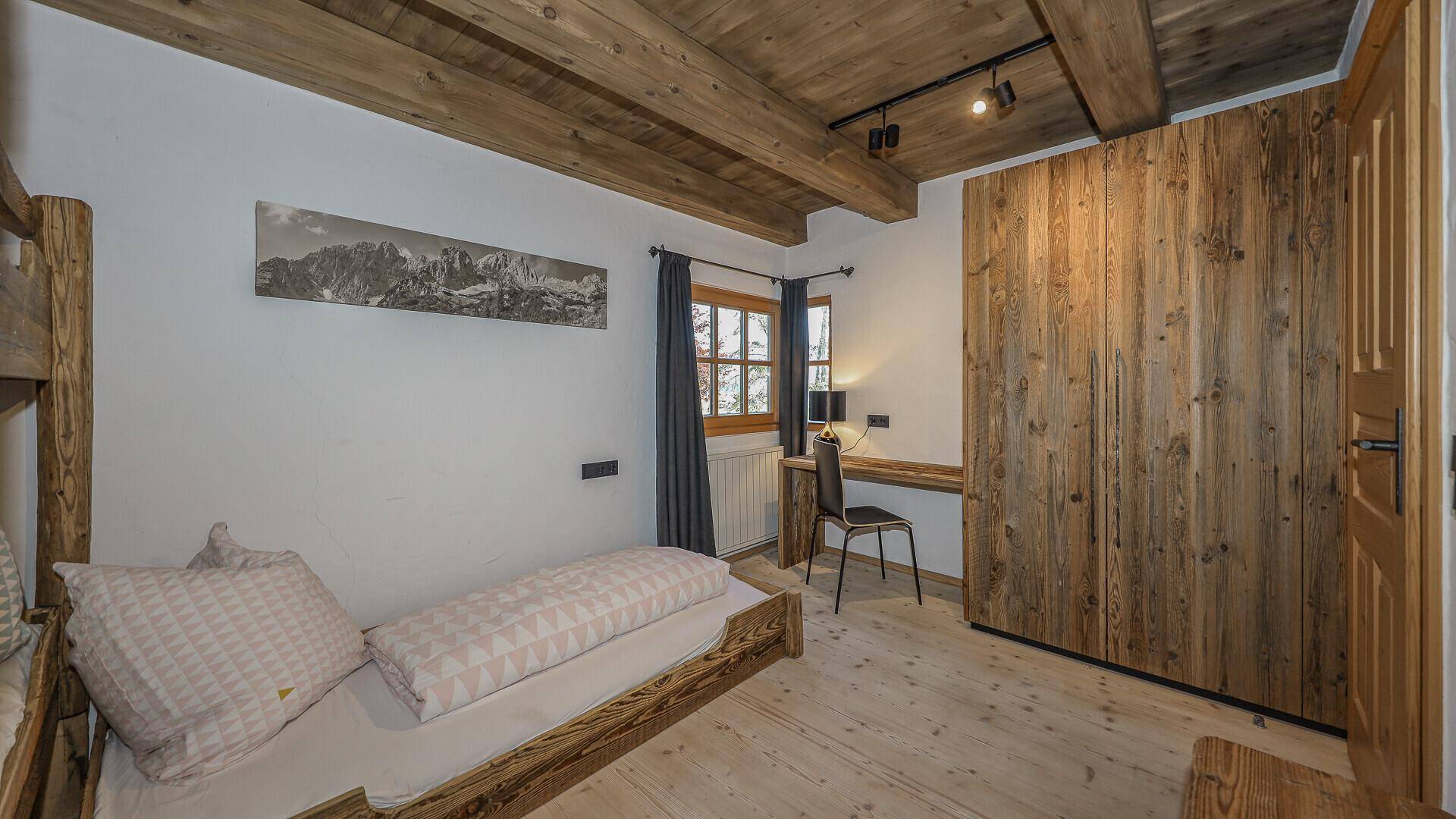 Helles Kinderzimmer mit Etagenbett, Schreibtisch und Holzschrank.