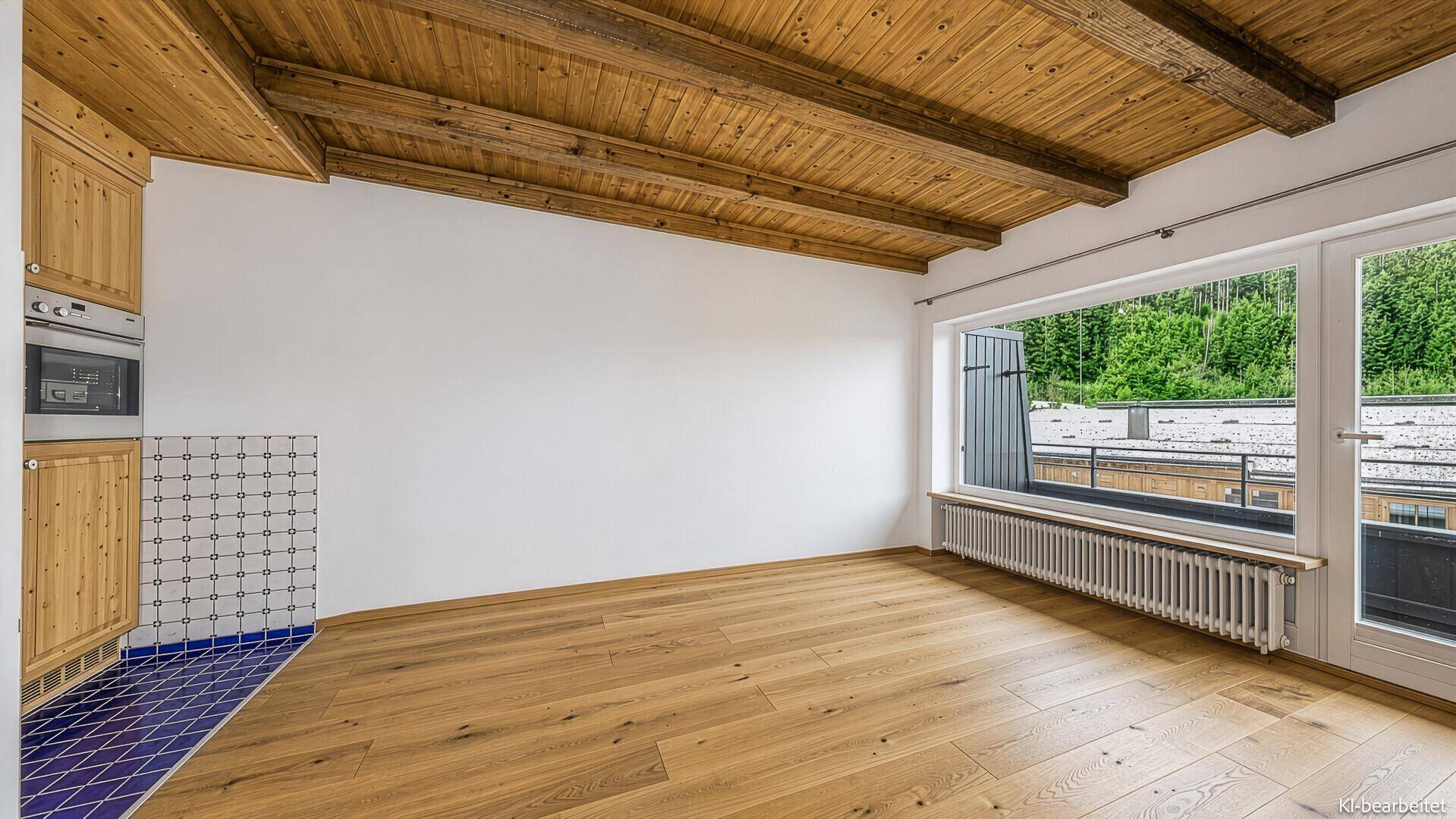 Heller Raum mit Holzbalkendecke, Parkettboden und einer kleinen Küchenzeile mit Fensterzugang.