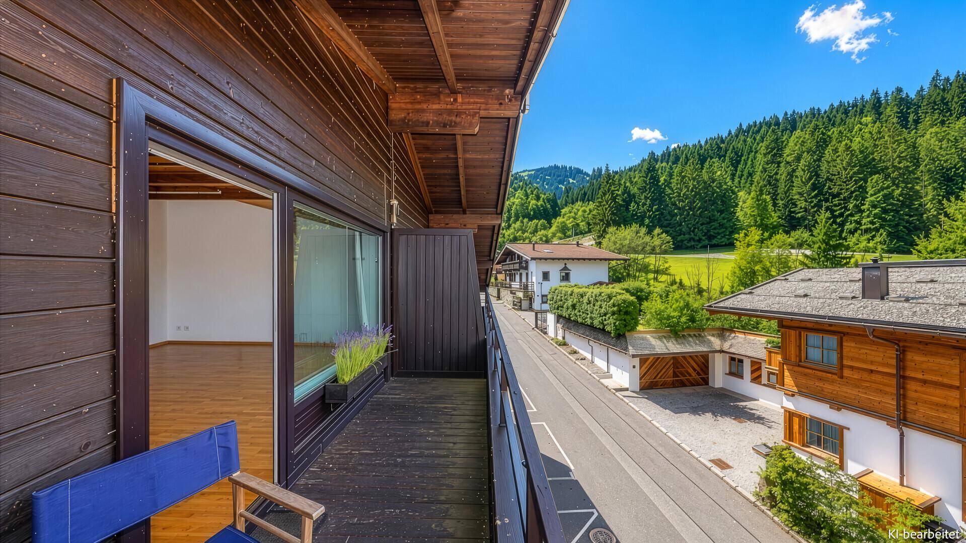 Langer Holzbalkon mit Blick auf die umliegende Natur und weitere Gebäude in der Ferne.