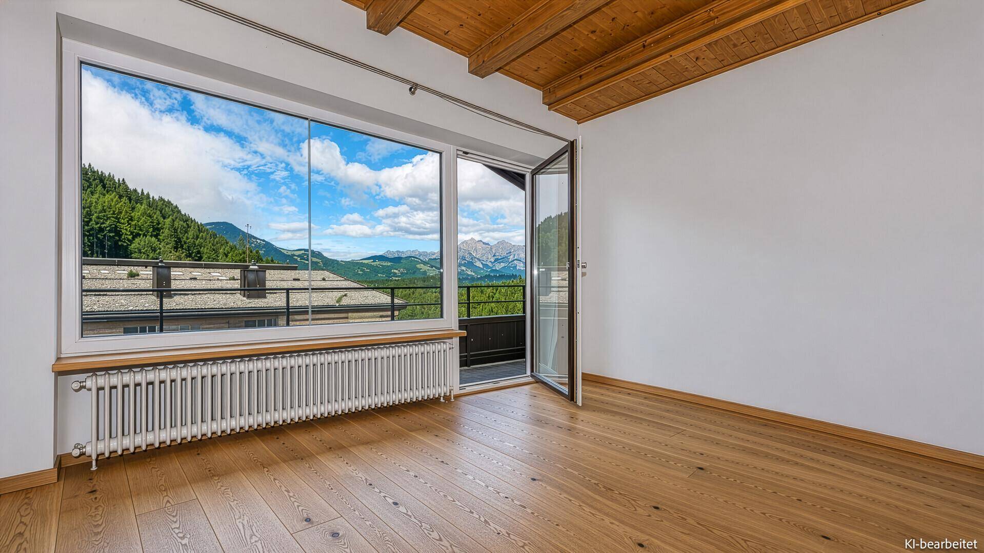 Leeres Zimmer mit Holzbalkendecke, Parkettboden und Zugang zu einem Balkon mit Bergblick.