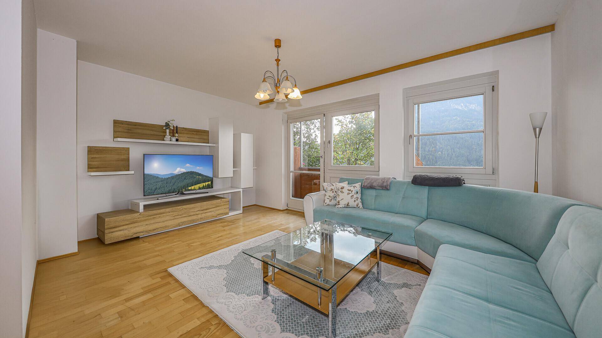 Helles Wohnzimmer mit hellblauem Ecksofa, Holzboden und Blick ins Grüne.