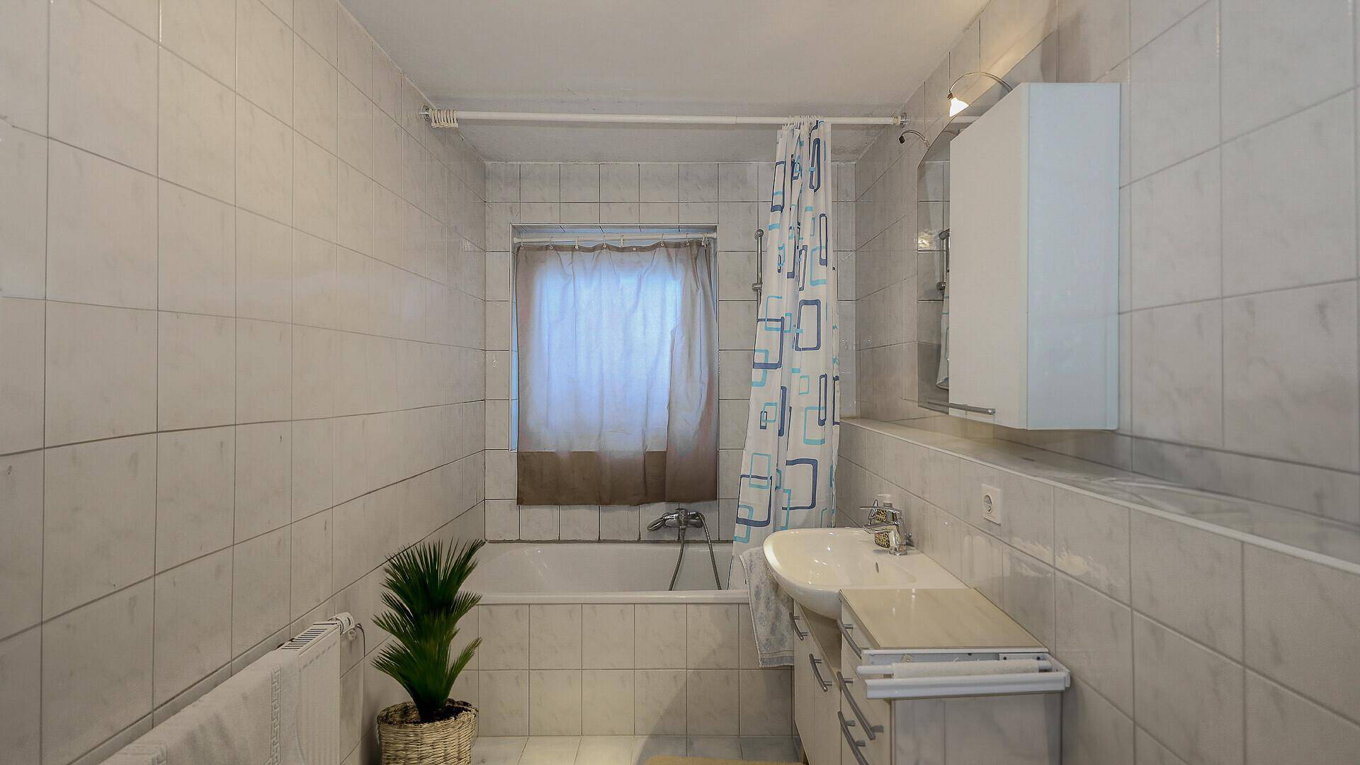 Helles Badezimmer mit Badewanne, Fliesen und Fenster.