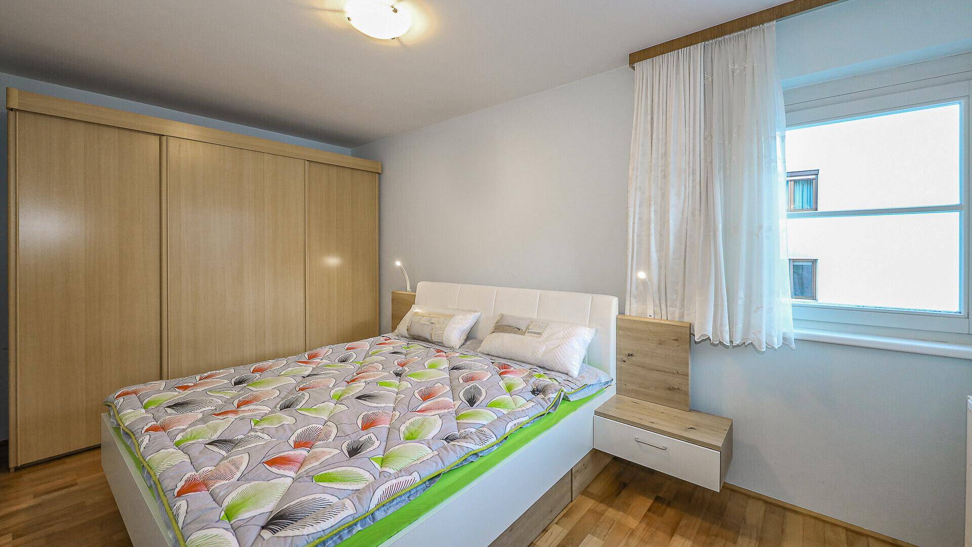 Helles Schlafzimmer mit Holzboden, Einbauschrank und Fenster.