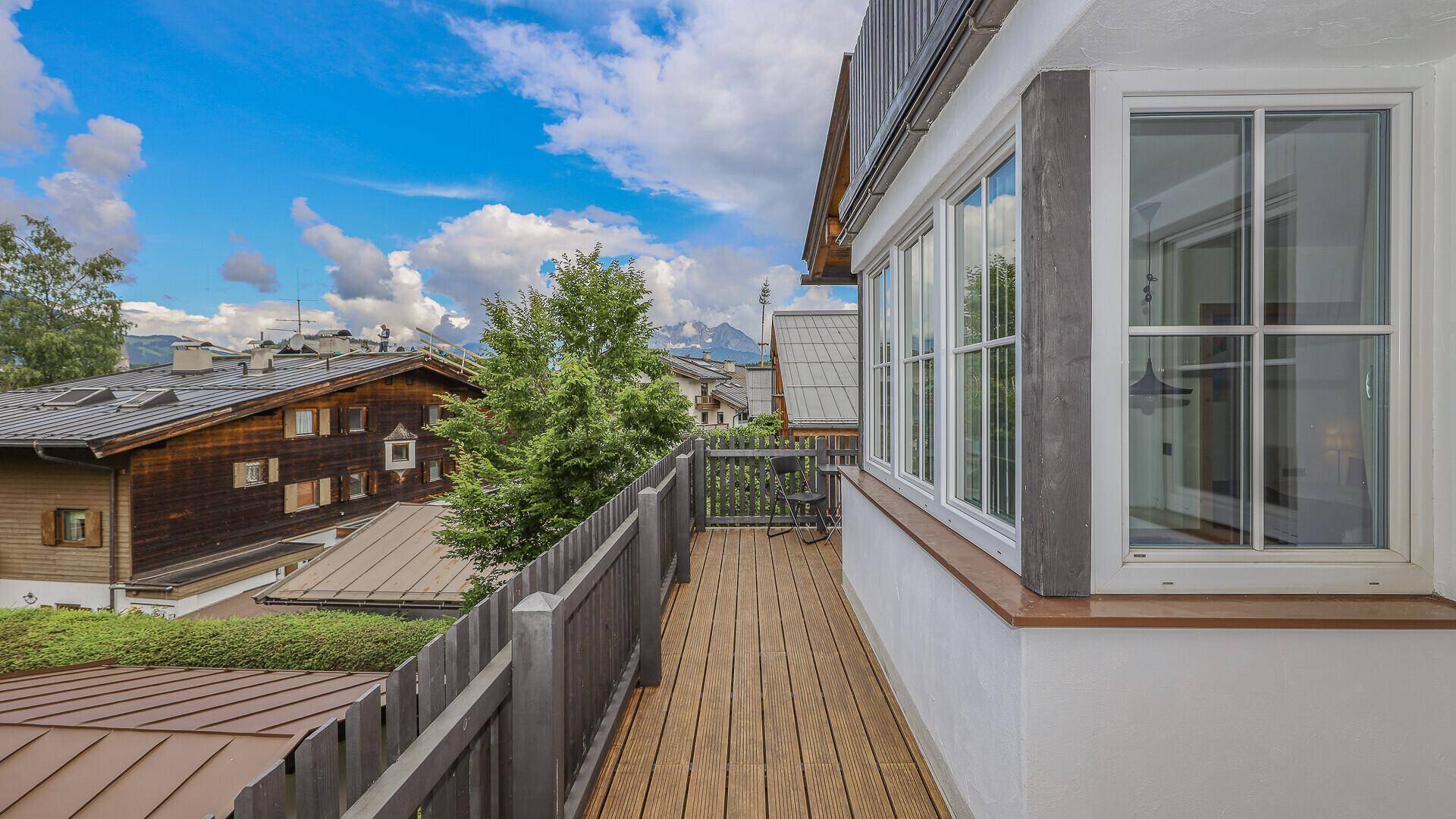 Langer Holzbalkon mit Blick auf die umliegenden Häuser und die Bergkulisse.