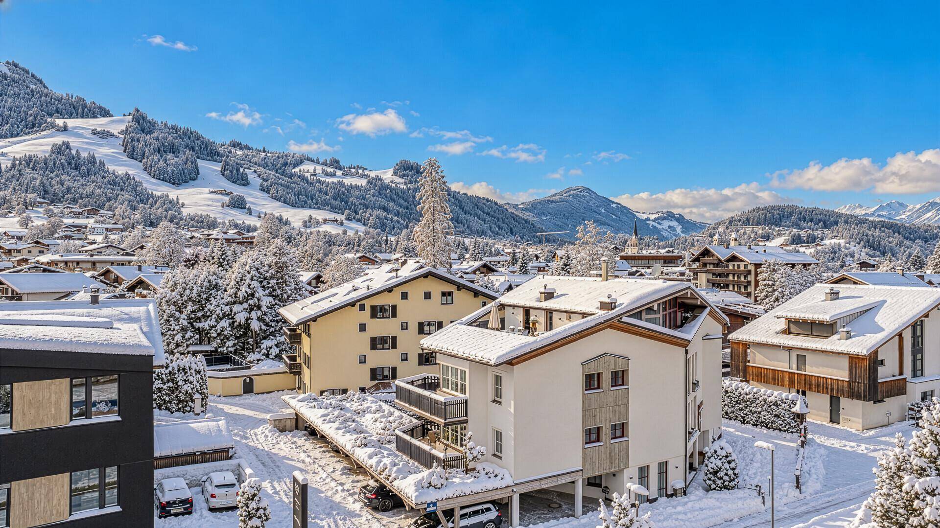 Winterlandschaft mit verschneiten Häusern und Bergen unter blauem Himmel.