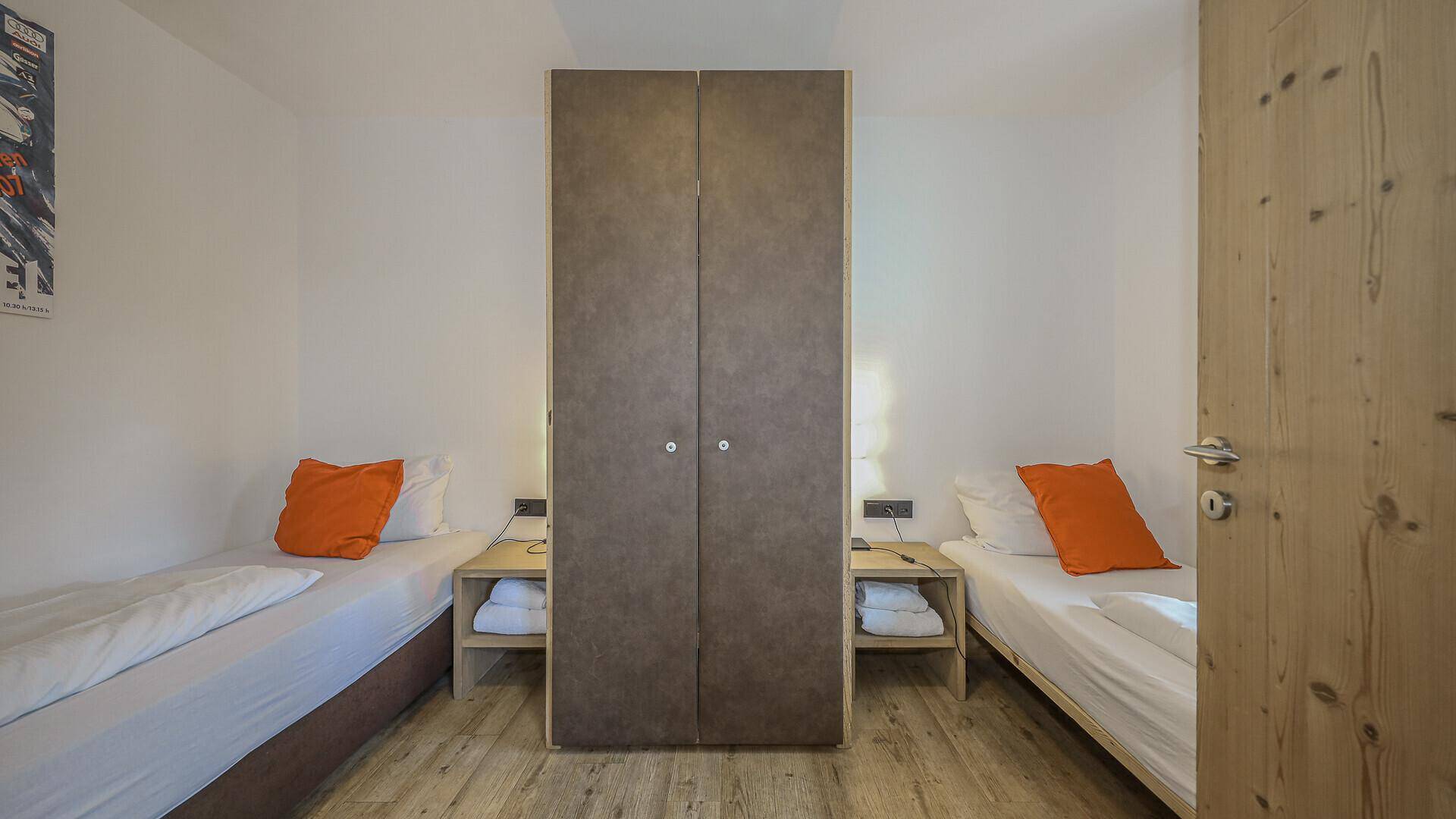 Schlafzimmer mit zwei Einzelbetten und einem Kleiderschrank, schlicht eingerichtet.