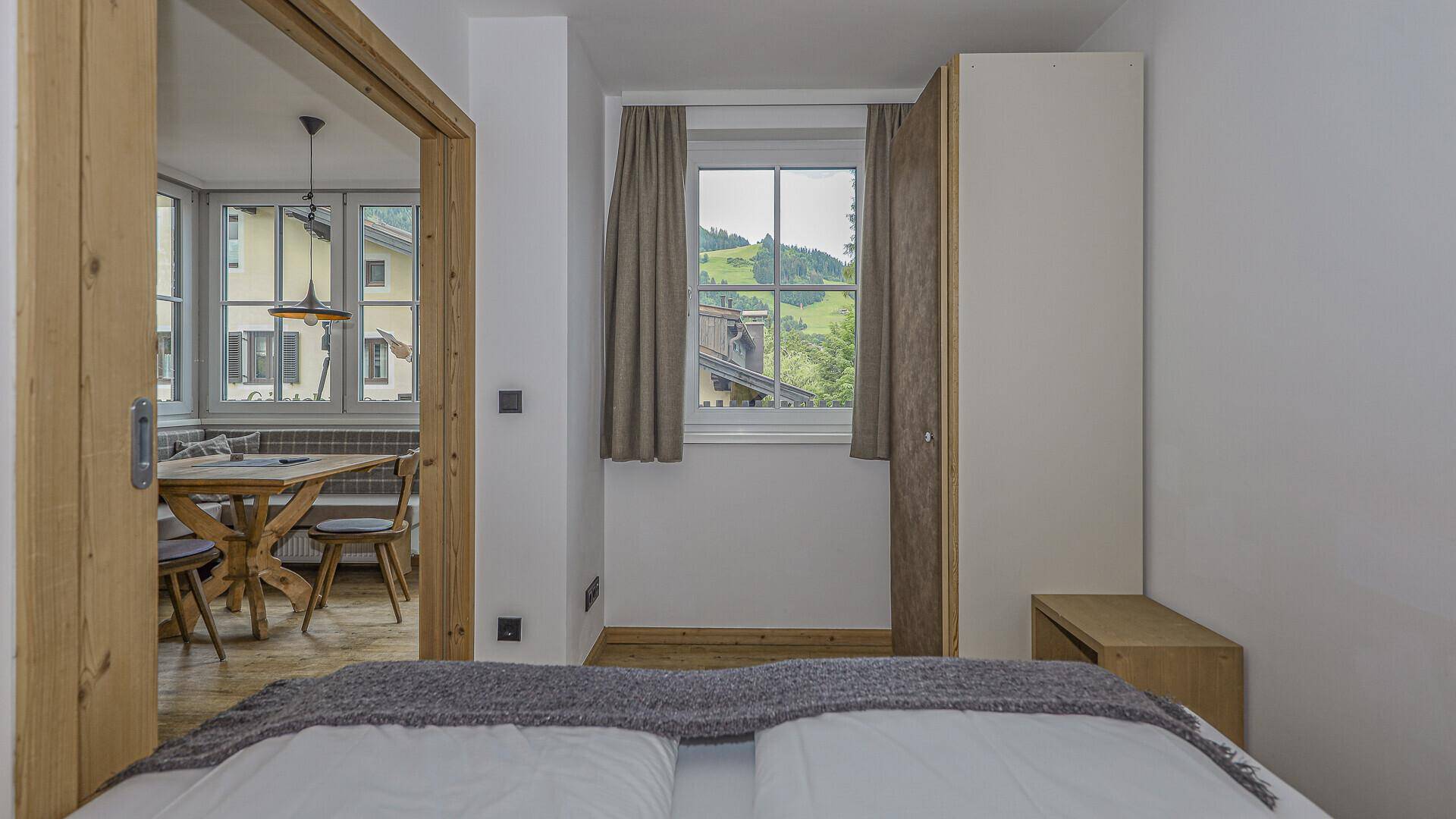 Schlafzimmer mit Fenster und Blick ins Grüne, angrenzend an einen Essbereich.
