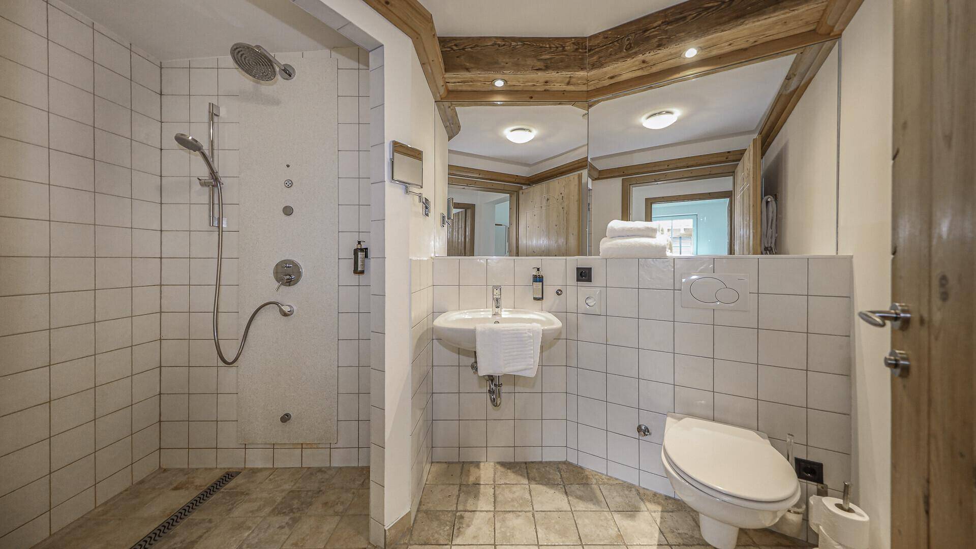 Modernes Badezimmer mit begehbarer Dusche, Waschbecken und WC, hell gefliest.