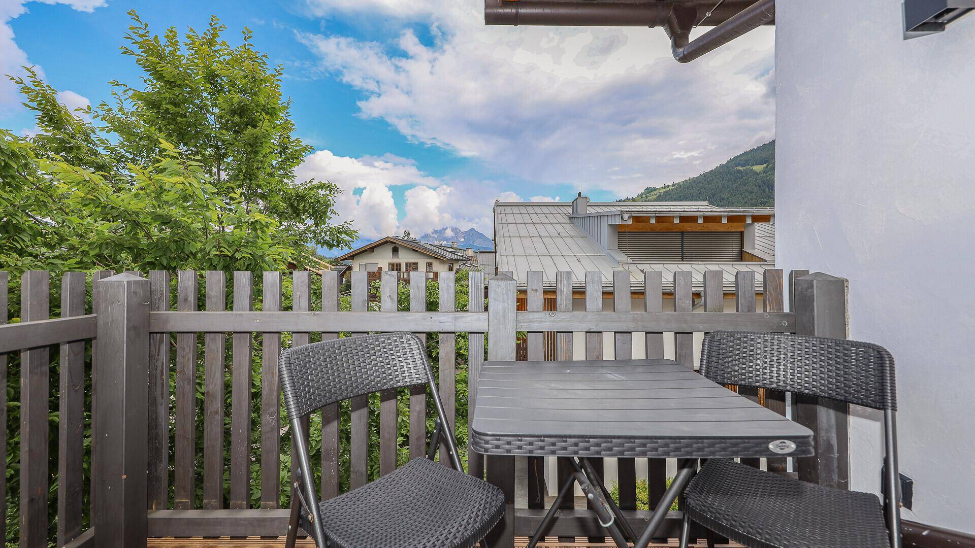 Gemütlicher Balkon mit Tisch und Stühlen, umgeben von grüner Natur und Bergblick.