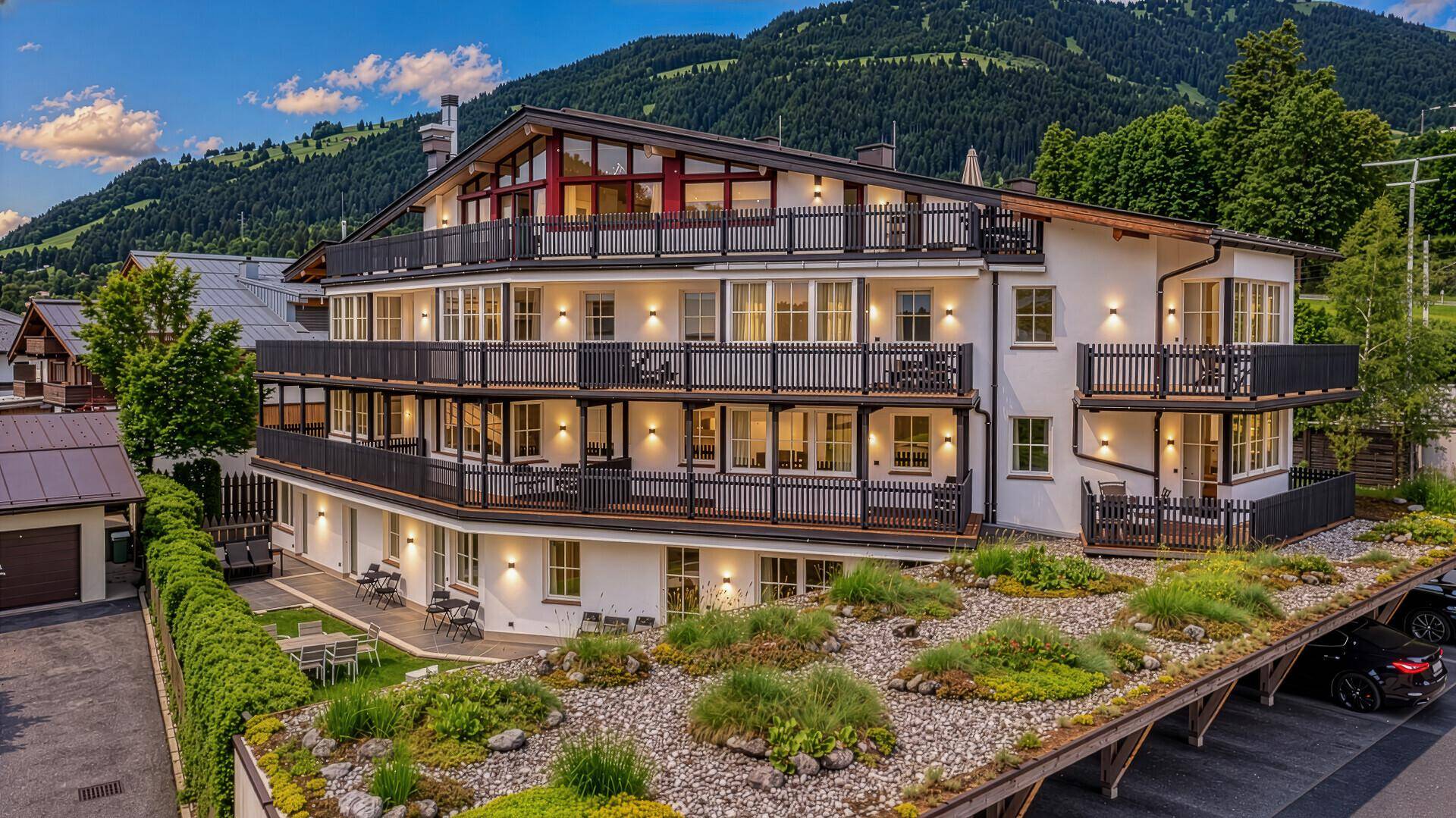 Modernes Mehrfamilienhaus mit mehreren Balkonen und begrüntem Dach in alpiner Umgebung.