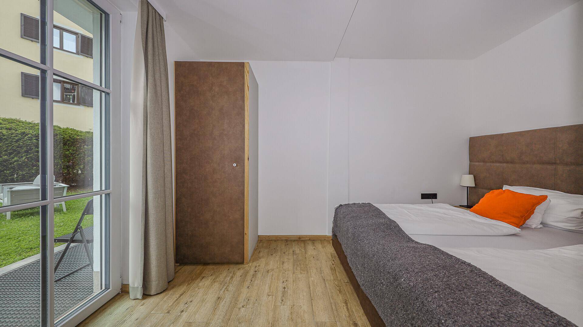 Schlafzimmer mit Doppelbett, Holzboden und Zugang zu einem kleinen Außenbereich oder Garten.