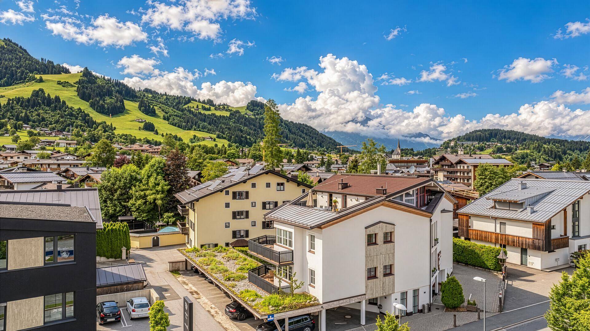 Panoramablick auf die alpine Siedlung mit mehreren Gebäuden und grünen Bergen im Hintergrund.