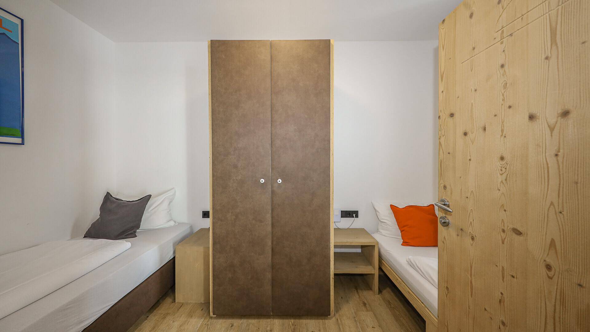Schlafzimmer mit zwei Einzelbetten, Holzboden und einem Kleiderschrank in der Mitte des Raumes.
