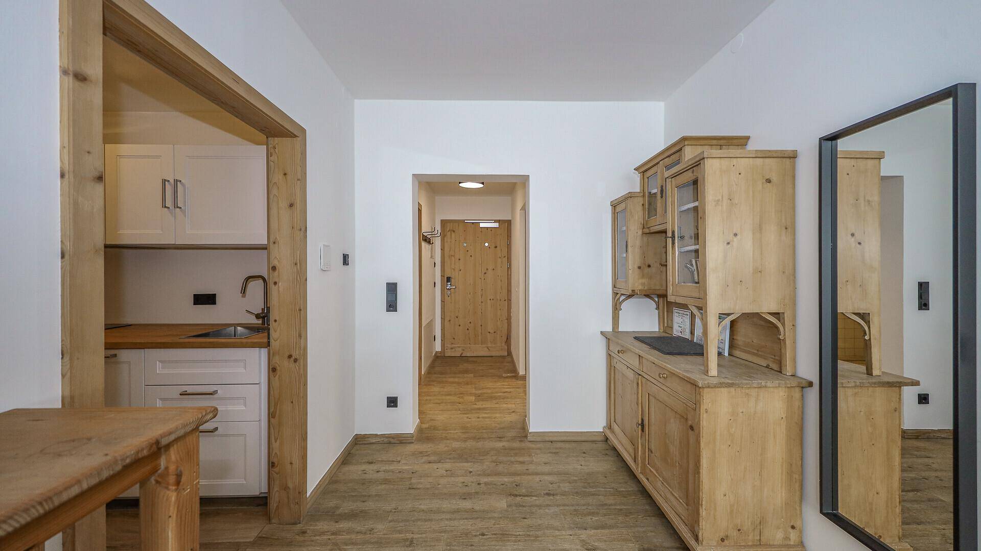 Heller Flur mit Holzboden und traditionellen Holzmöbeln, der zu einer kleinen Küchenzeile führt.