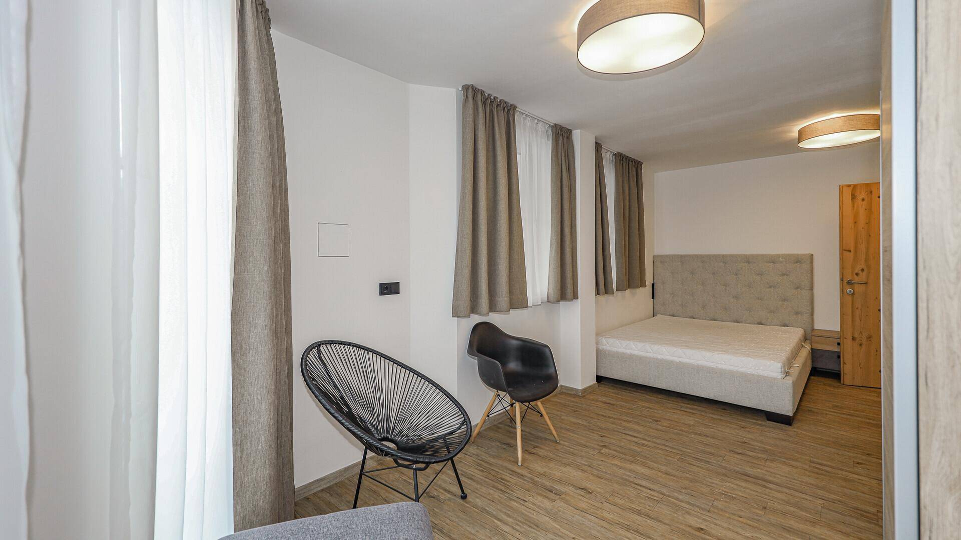 Helles Schlafzimmer mit Doppelbett, Holzboden und modernen Stühlen, durchflutet von Tageslicht.