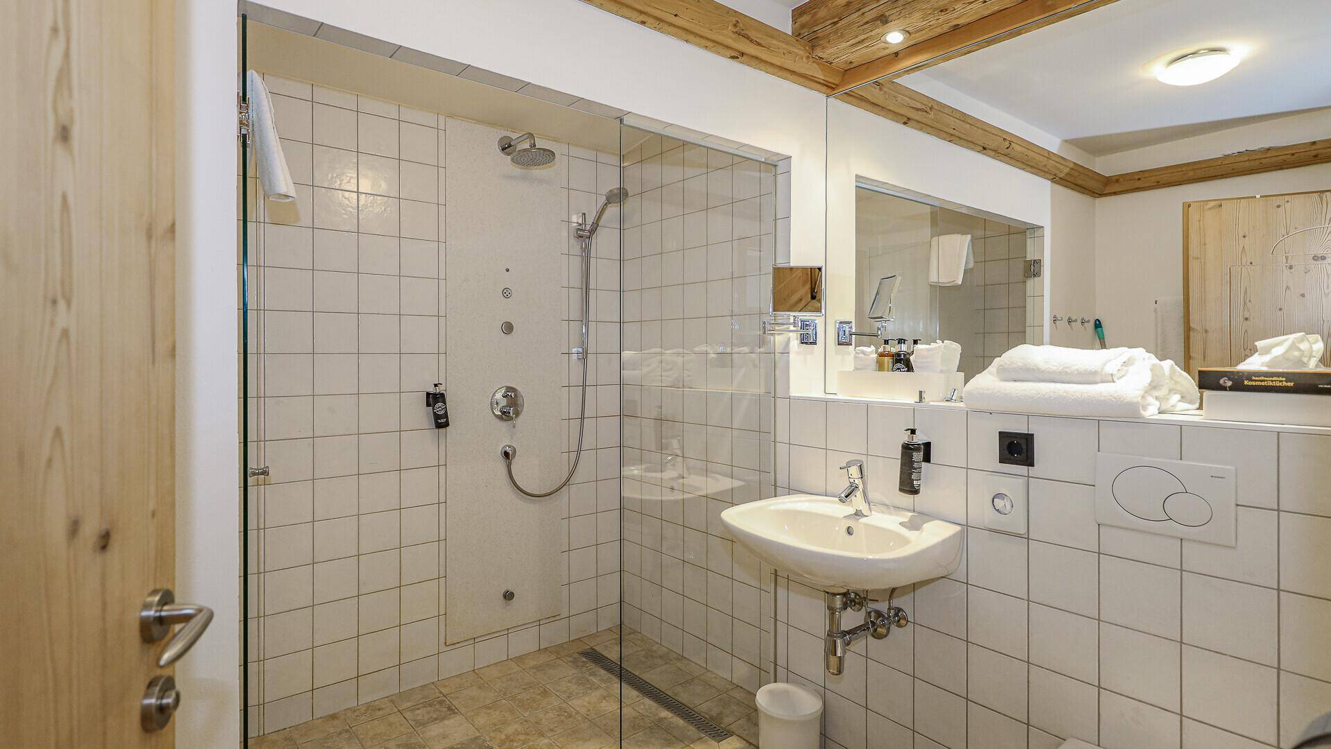 Modernes Badezimmer mit großer begehbarer Dusche, Waschbecken und Holzbalken an der Decke.