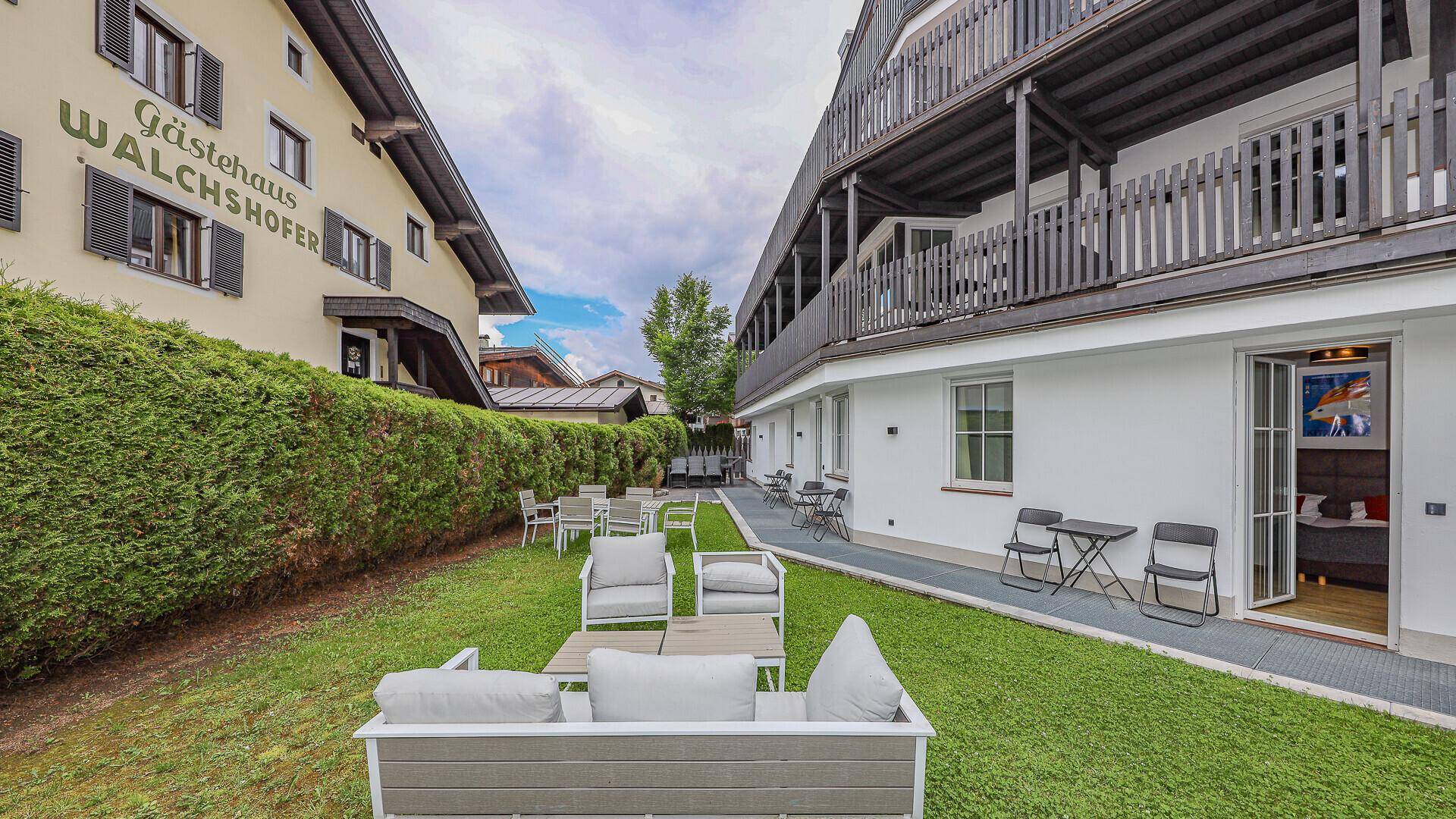 Weitläufiger Gartenbereich mit verschiedenen Sitzgelegenheiten und Blick auf die umliegenden Gebäude.